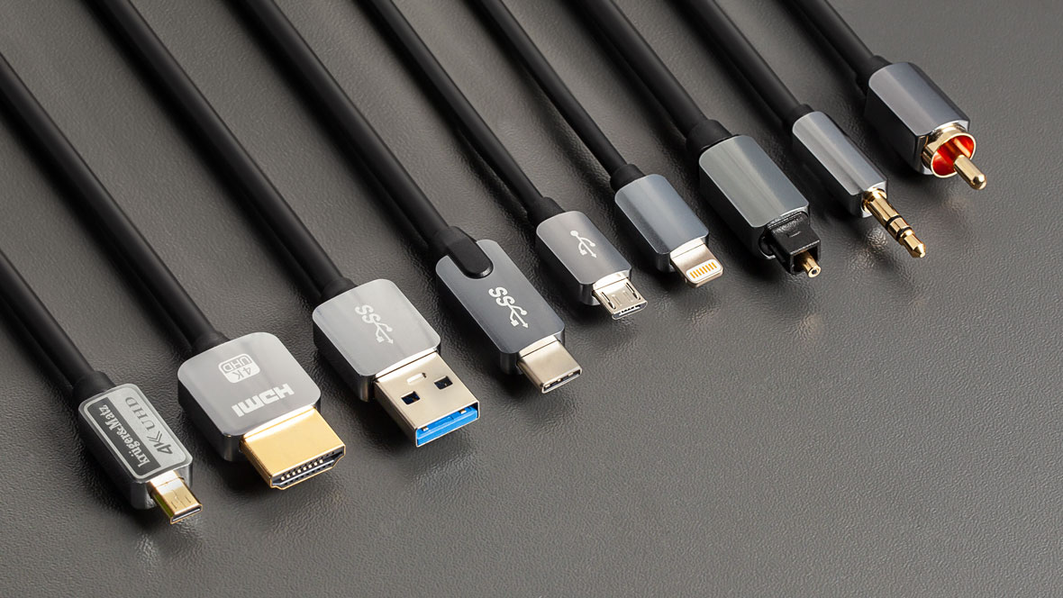 Różne czarne kable z różnymi złączami, takimi jak HDMI, USB i jack, na szarym tle.