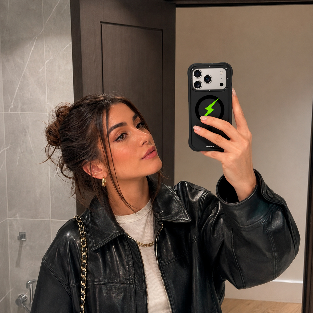 Una mujer con chaqueta de cuero negra se hace un selfi frente al espejo con un smartphone negro con un rayo verde.