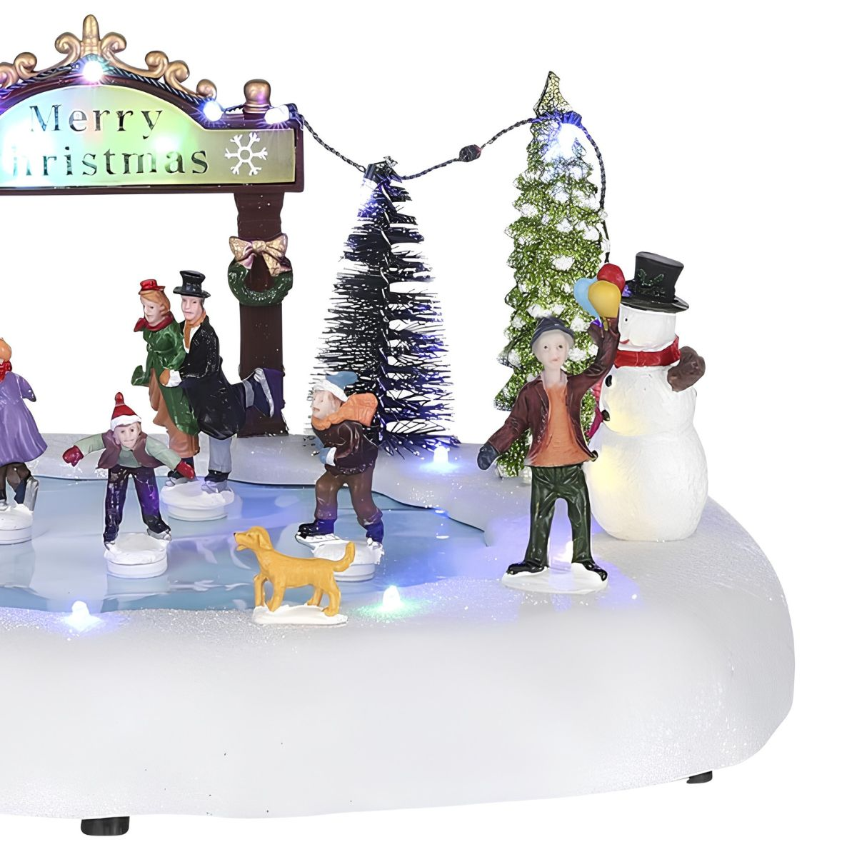 Figurine de village de Noël avec des patineurs, un chien et un bonhomme de neige devant un panneau Joyeux Noël lumineux.