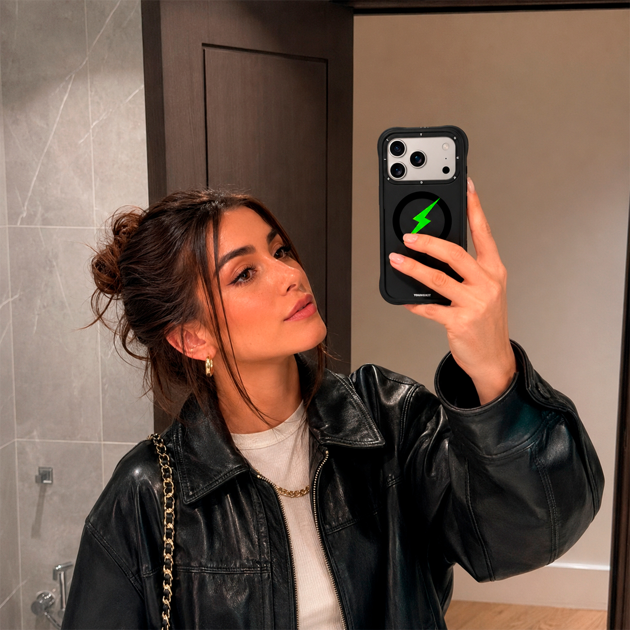 Una mujer con chaqueta de cuero se hace un selfie frente al espejo con un smartphone.