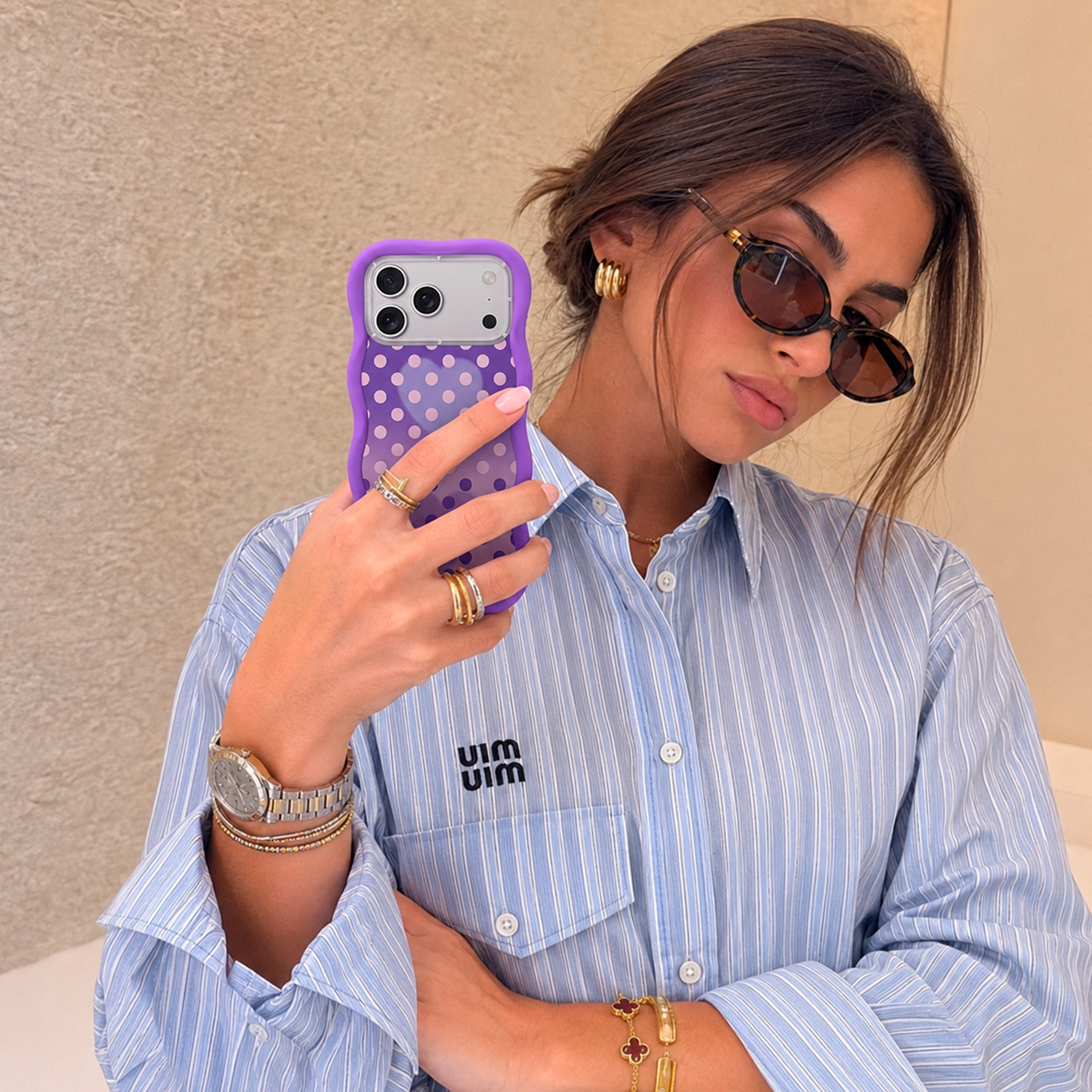 Una mujer con camisa a rayas azules, gafas de sol y funda de móvil morada.