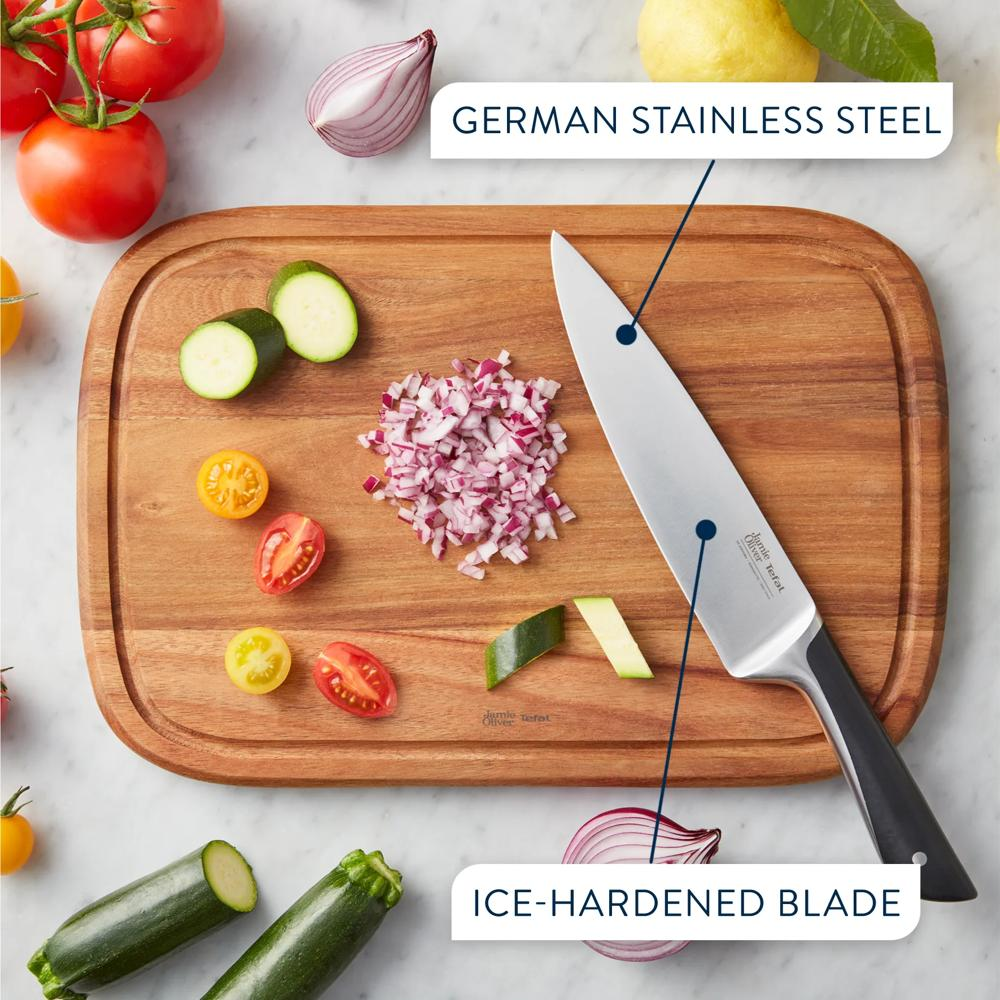 Ein hölzernes Schneidebrett mit gehackten Zwiebeln, Tomaten und Zucchini sowie einem deutschen Edelstahlmesser.