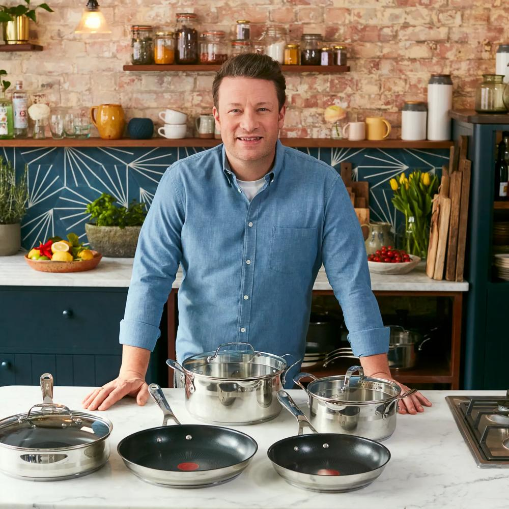 Jamie Oliver steht in einer Küche hinter einer Küchentheke mit Kochgeschirr.