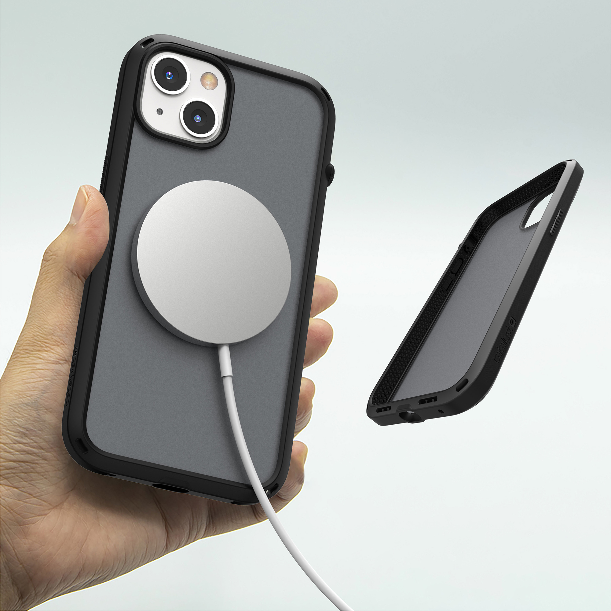 Hand hält iPhone mit schwarzer Hülle und MagSafe-Ladegerät, eine zweite Hülle schwebt rechts.