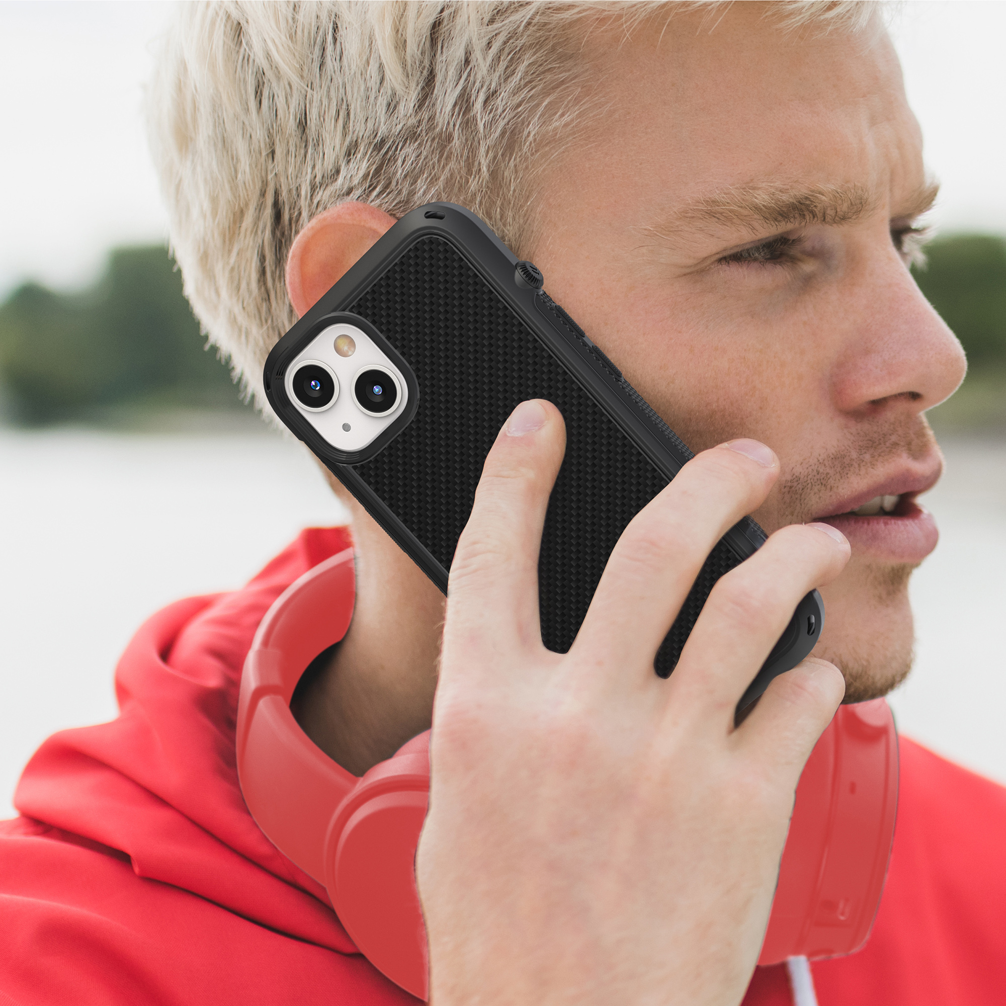 Ein blondhaariger Mann telefoniert mit einem schwarzen Smartphone und trägt rote Kopfhörer.