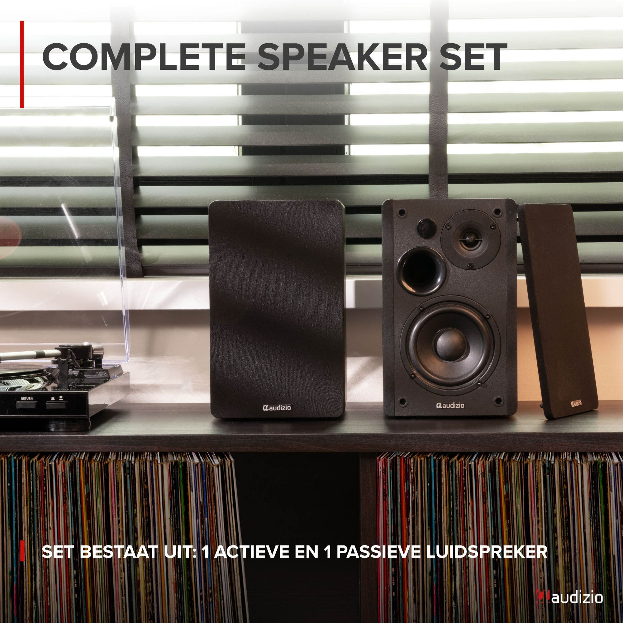 Un juego de altavoces negros en un estante con discos de vinilo, junto a un tocadiscos frente a persianas.