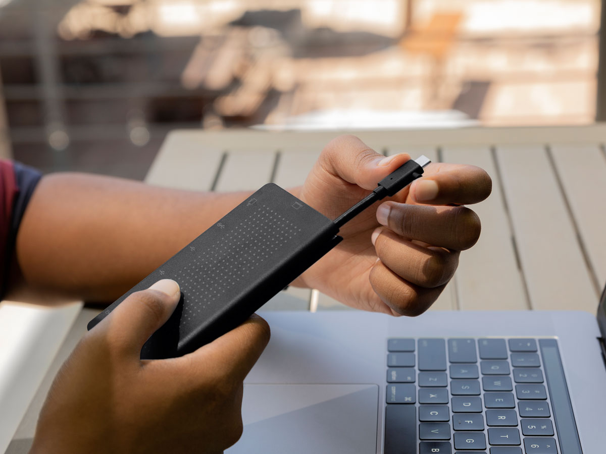 Eine Person hält eine schwarze externe SSD mit integriertem USB-C-Kabel über einen Laptop.