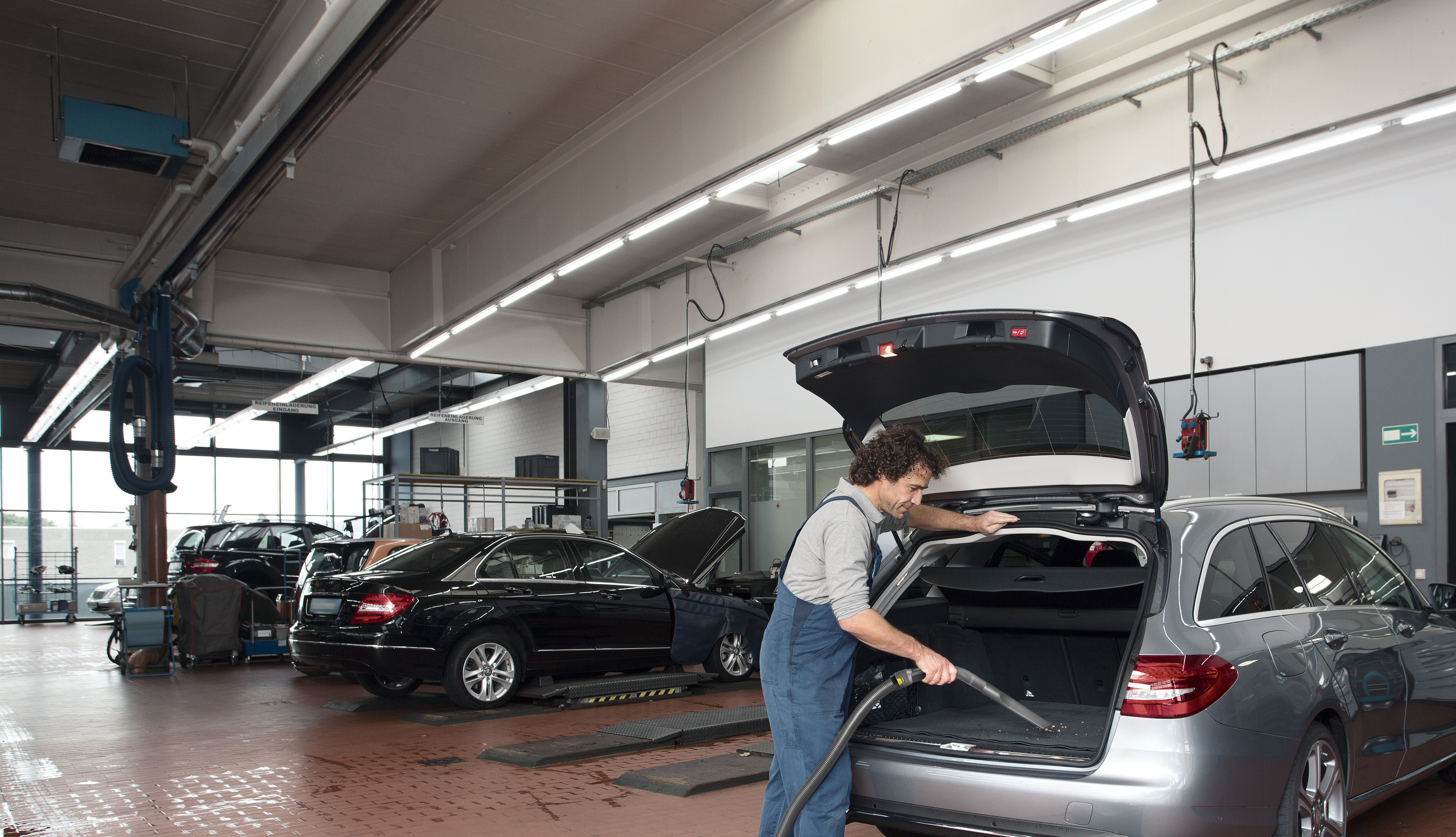 Mechanik w niebieskich ogrodniczkach odkurza bagażnik srebrnego kombi w dobrze oświetlonym warsztacie.