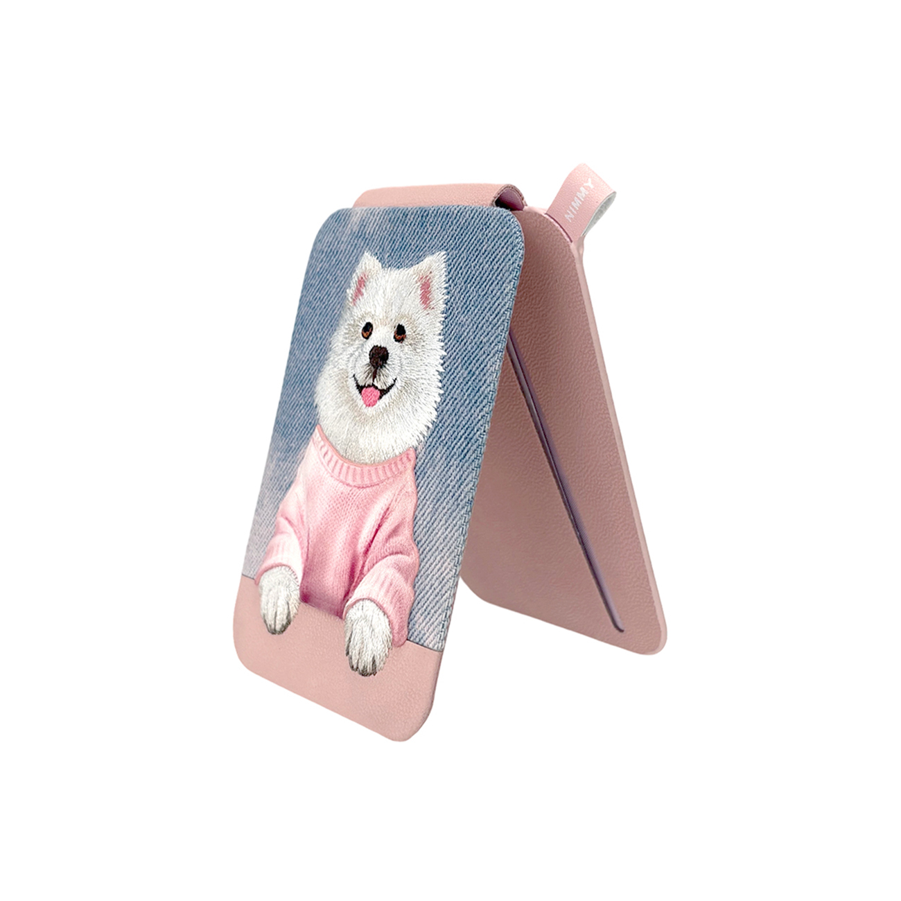 Un soporte para teléfono de cuero rosa muestra un perro blanco bordado con suéter rosa sobre fondo de mezclilla azul.