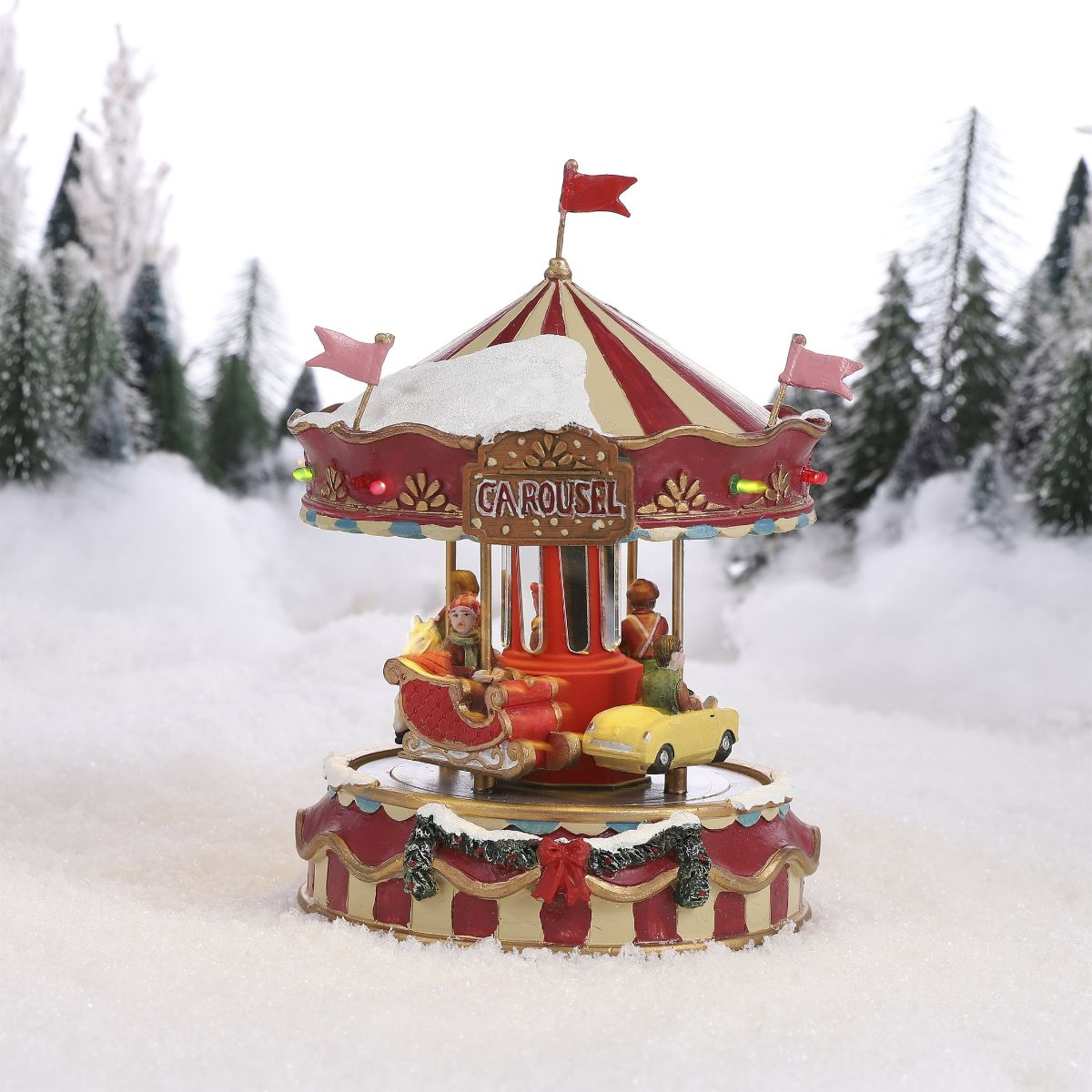 Een rood-wit gestreepte kerstcarrousel in de sneeuw, omringd door besneeuwde dennenbomen.