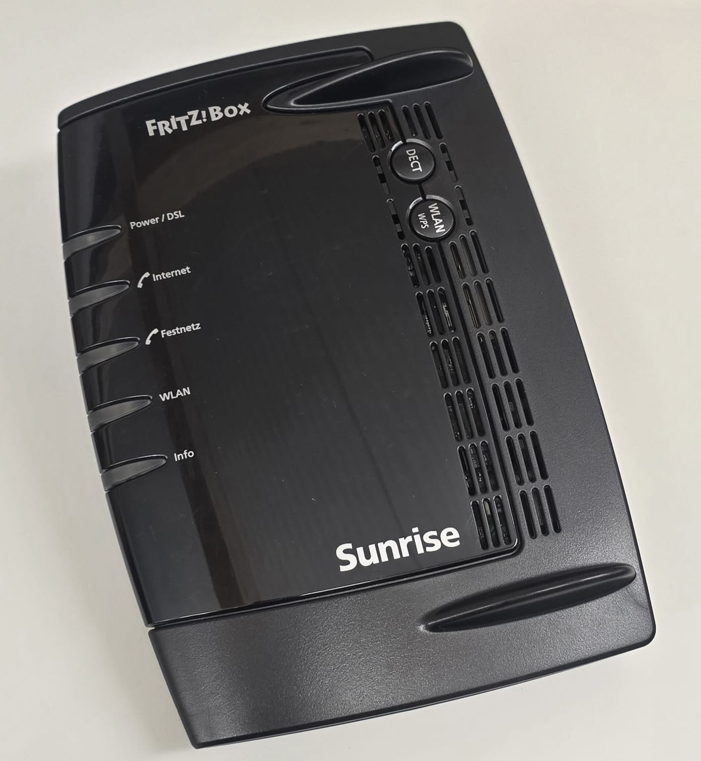 Schwarzer FRITZ!Box Router mit Sunrise Logo, DECT- und WLAN-Tasten sowie LED-Anzeigen auf hellem Hintergrund.