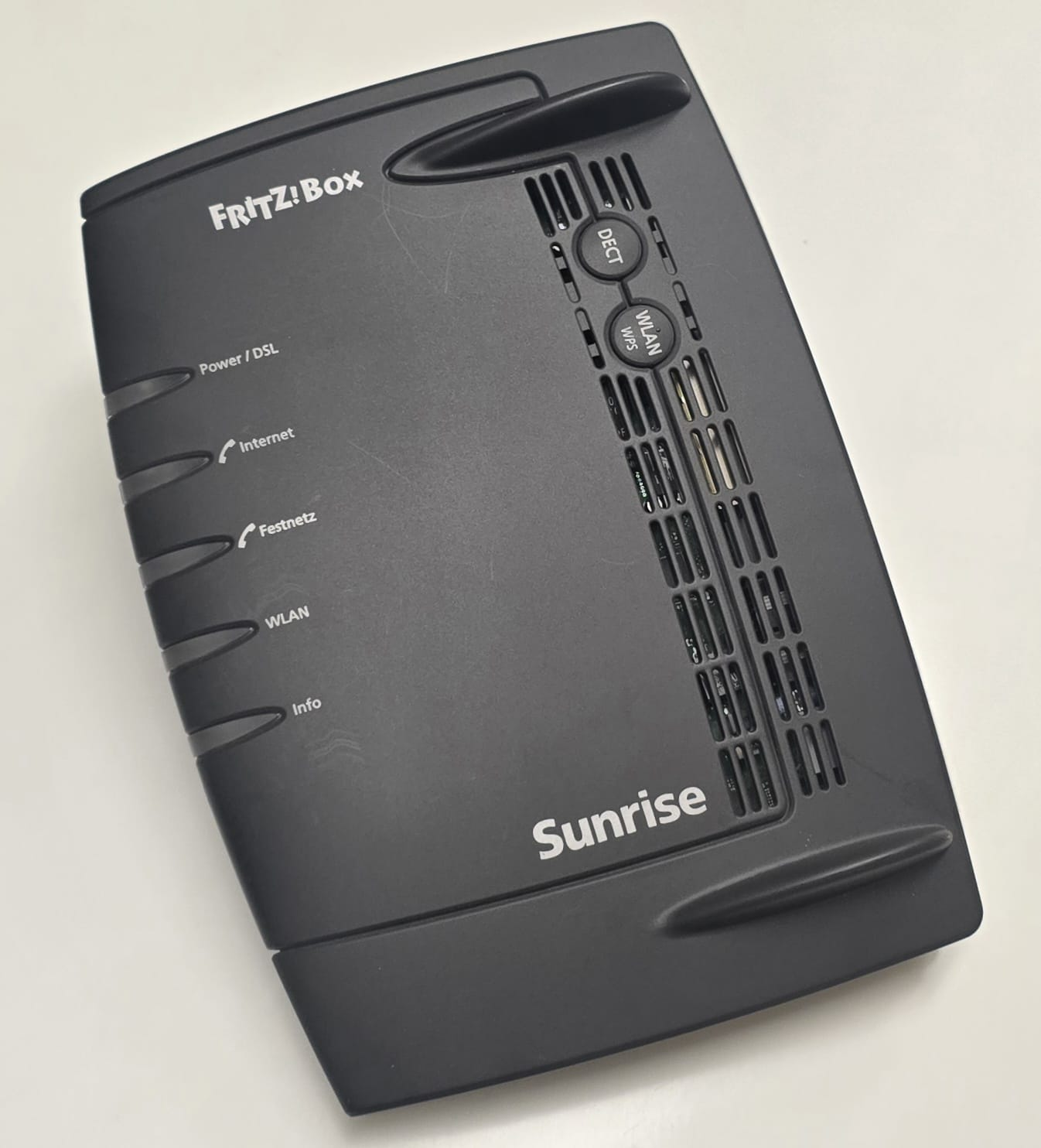 Ein schwarzer Fritz!Box-Router mit Sunrise-Branding, Statusleuchten und Lüftungsschlitzen auf weißer Oberfläche.