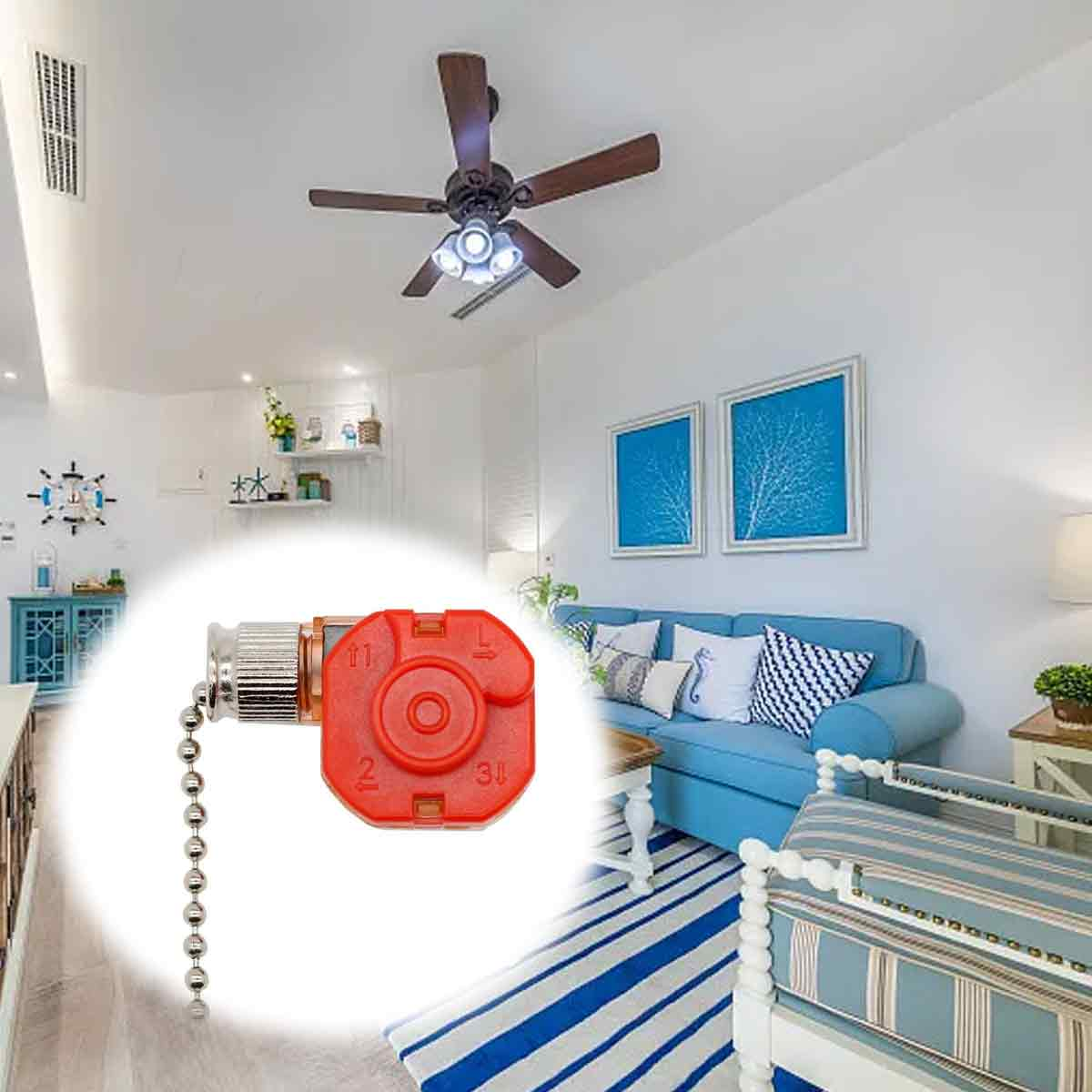 Ein roter Deckenventilatorschalter mit Zugkette im Vordergrund vor einem hellen Wohnzimmer mit blauem Sofa.