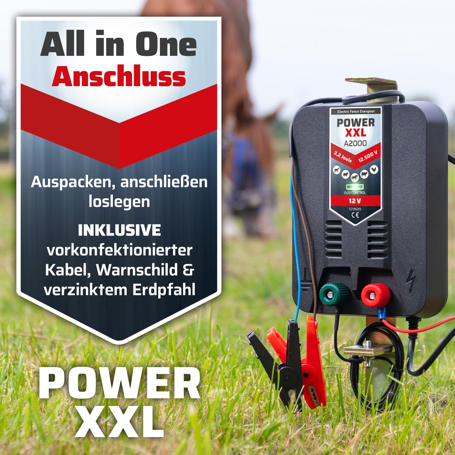 Électrificateur de clôture POWER XXL A2000 sur un pré avec des pinces de câble rouges et noires.