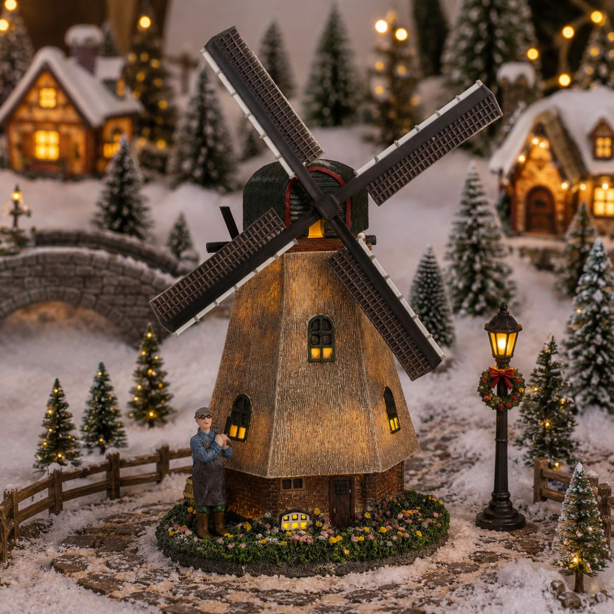 Verlichte molen in besneeuwd kerstdorp met beeldje en lantaarnpaal.
