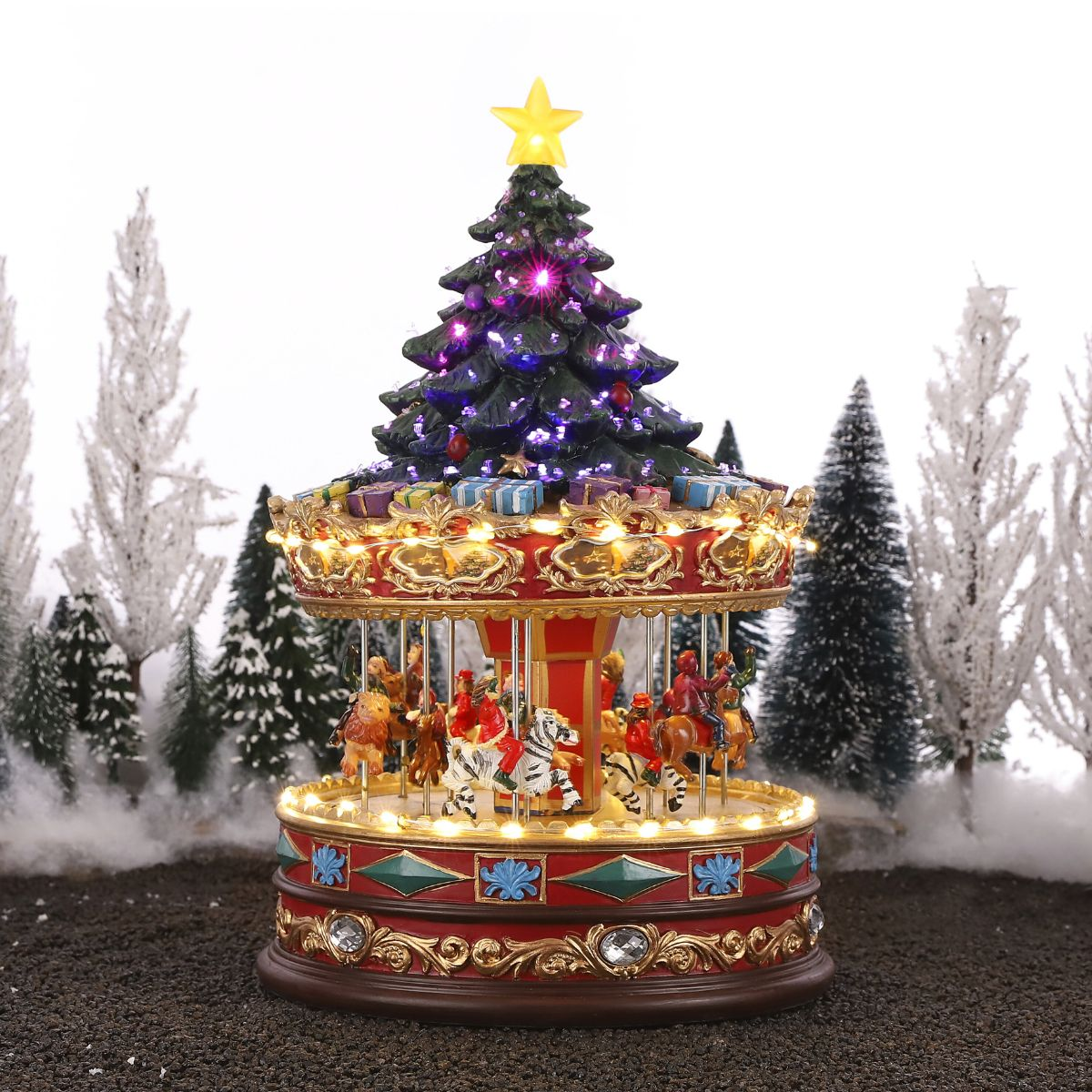 Een feestelijke carrousel speeldoos met kerstboom erop, omringd door besneeuwde dennenbomen.