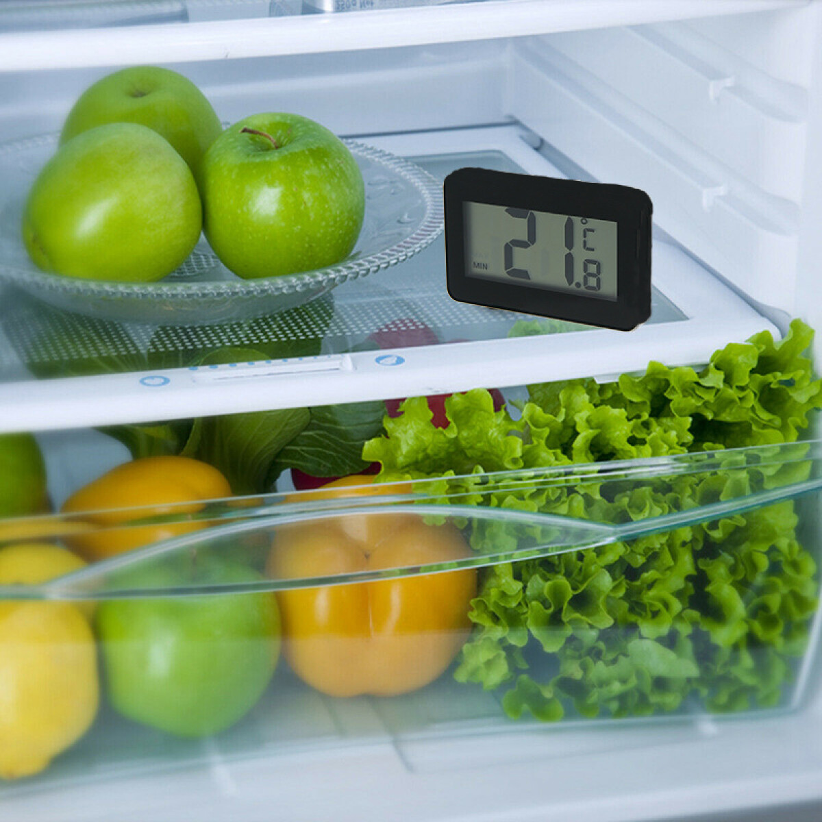 Kühlschrankinnenraum mit grünen Äpfeln oben, digitalem Thermometer und Gemüseschublade mit Salat und gelber Paprika.