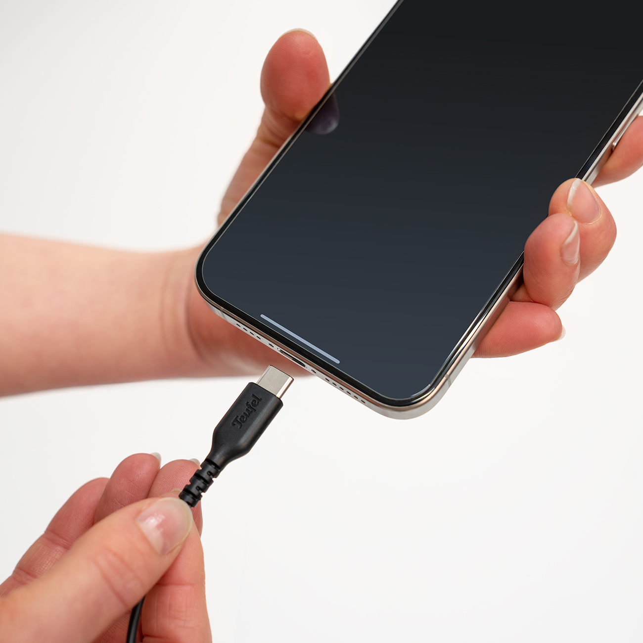 Eine Hand hält ein Smartphone, während eine andere Hand ein schwarzes Ladekabel mit der Ladebuchse verbindet.