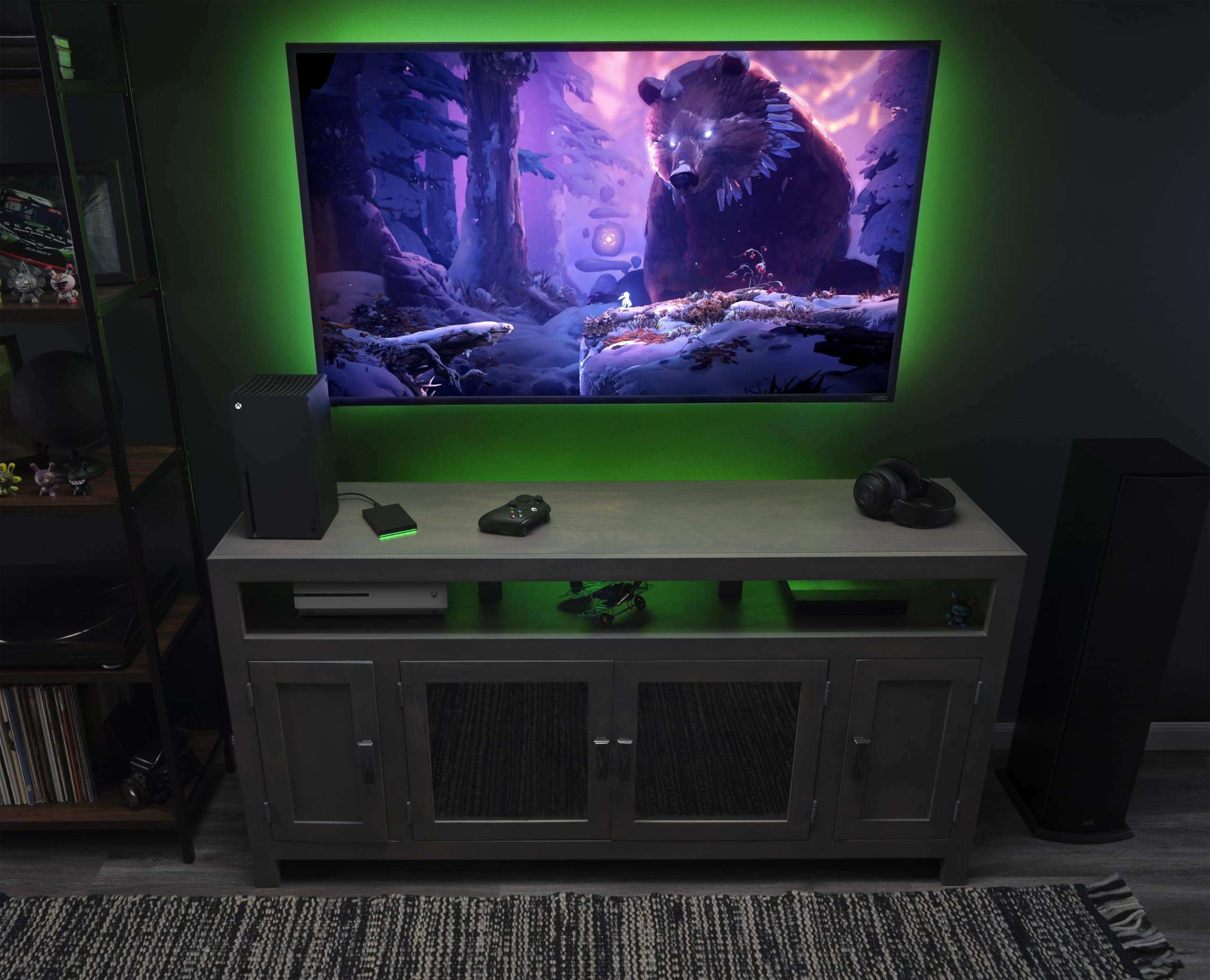 Ein Fernseher mit grünem LED-Hintergrundlicht zeigt einen Bären im Wald, auf einem grauen Medienschrank.