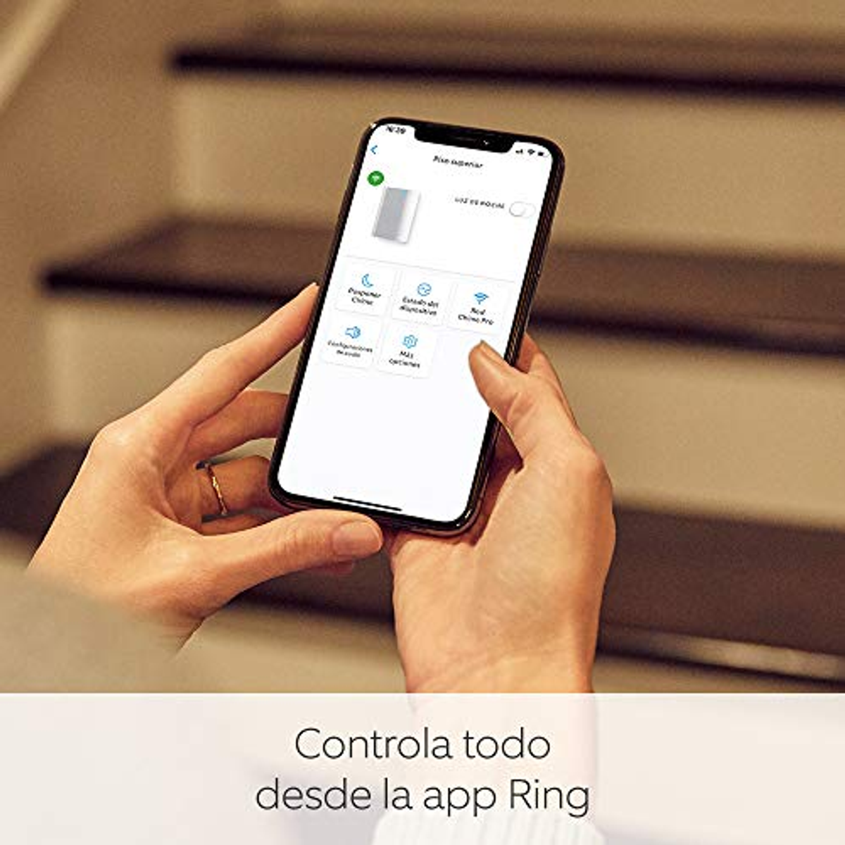 Mains tenant un smartphone affichant une application de maison intelligente, escaliers en arrière-plan.