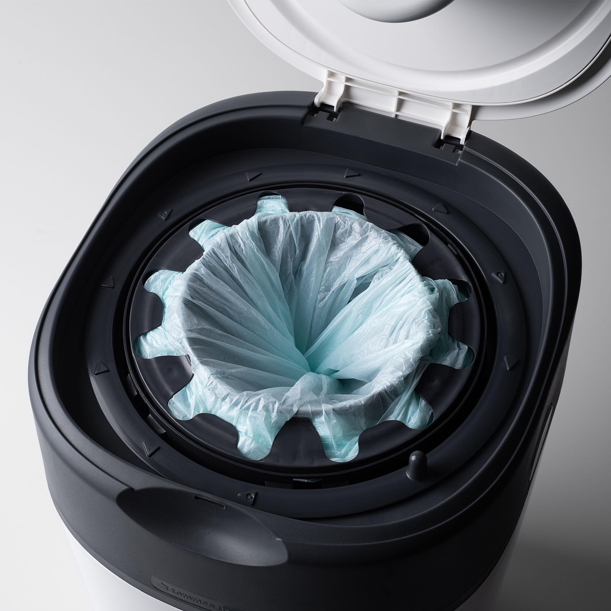 Ein offener weiß-grauer Windeleimer mit einer hellblauen Plastiktüte im inneren Ring.