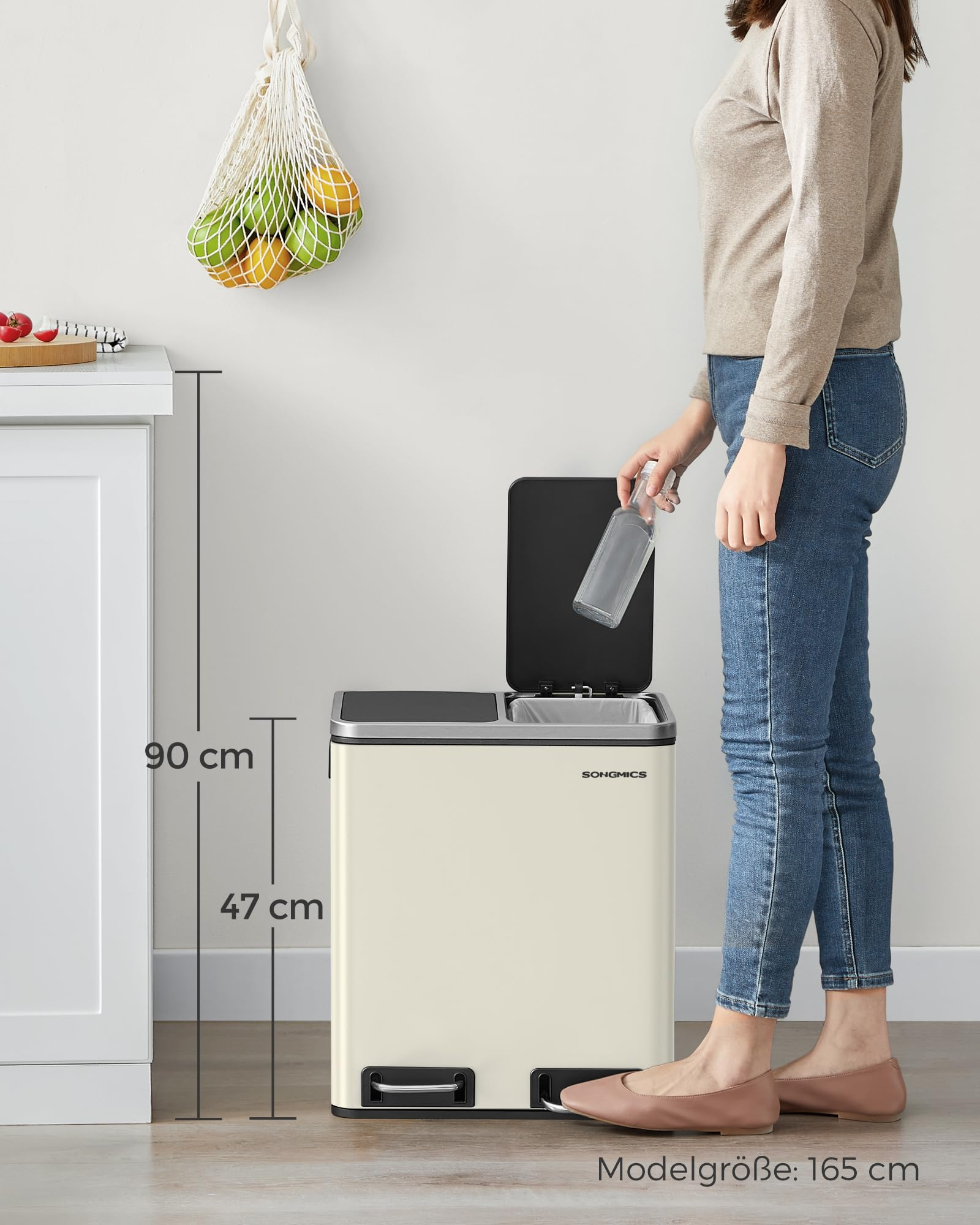 Une femme en jean jette une bouteille en verre dans une poubelle beige de cuisine.