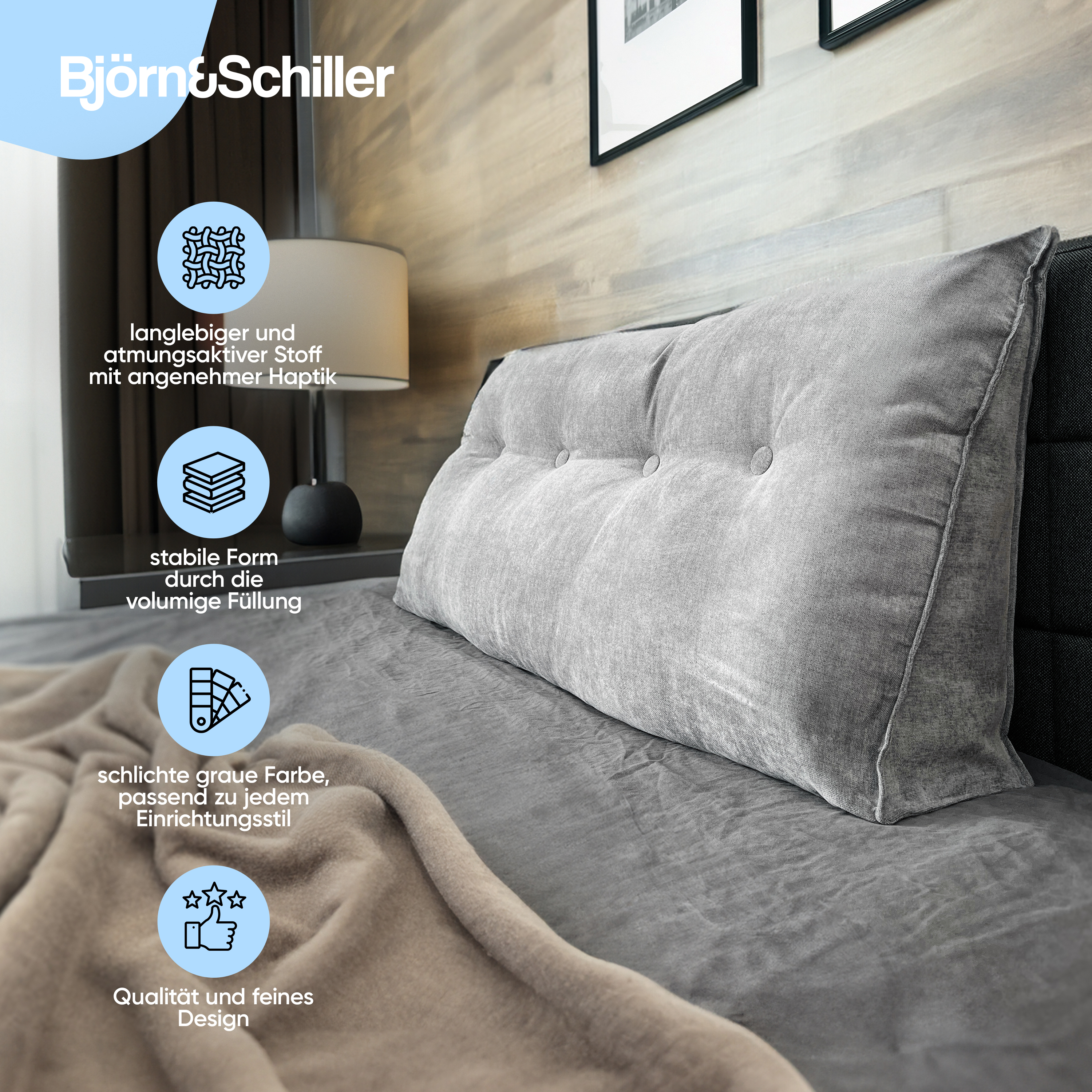 Ein großes graues Keilkissen auf einem Bett mit einer beige Decke neben einer Lampe.