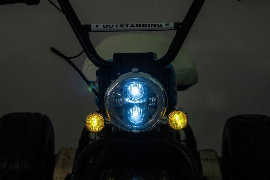 Nahaufnahme der Front eines Minibikes mit eingeschaltetem blauen Hauptscheinwerfer und zwei gelben Lichtern.