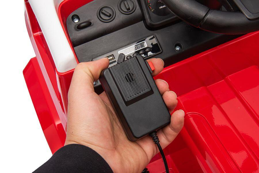 Eine Hand hält ein schwarzes Mikrofon vor dem Armaturenbrett eines roten Spielzeugautos.