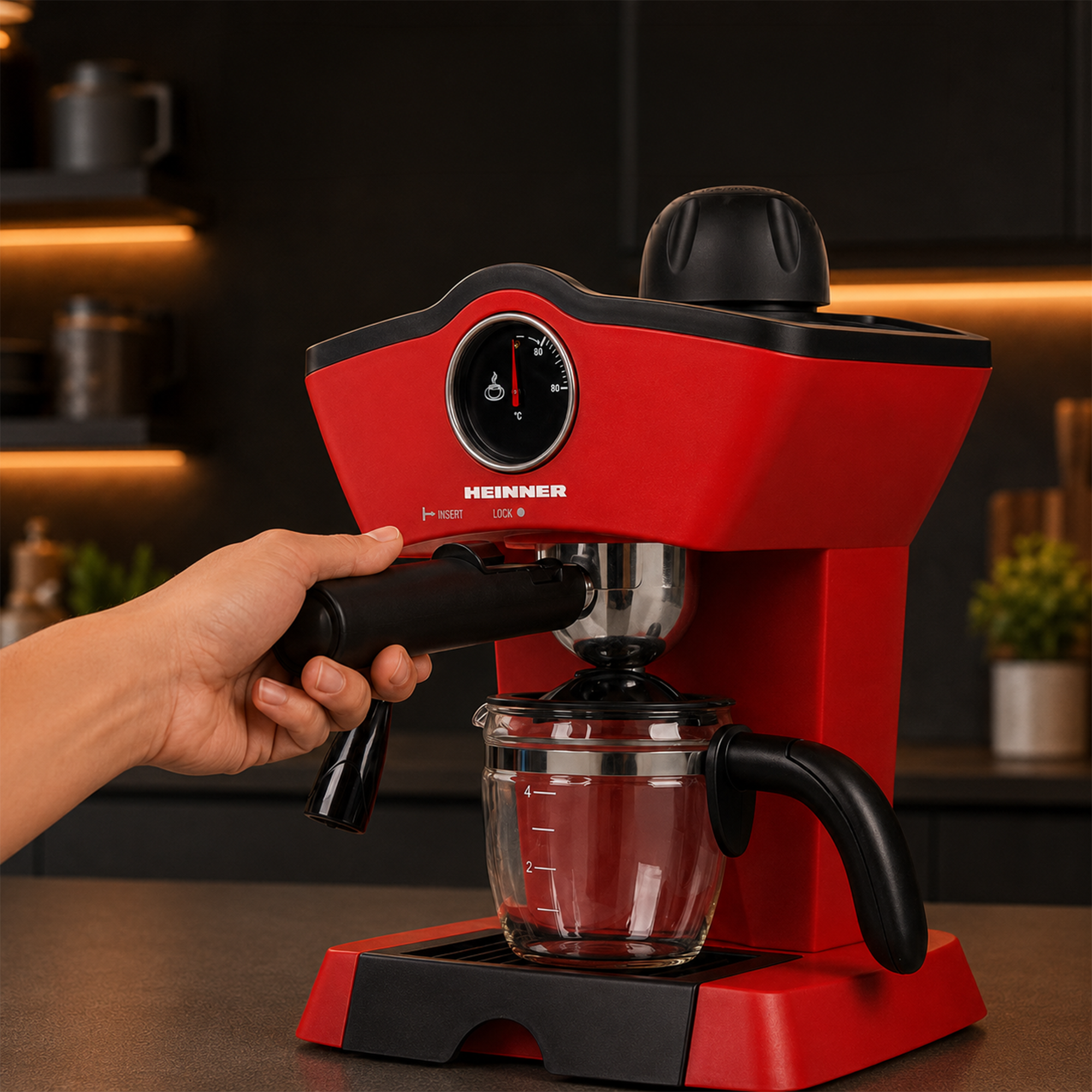 Une main insère le porte-filtre dans une machine à espresso Heinner rouge dans une cuisine sombre.