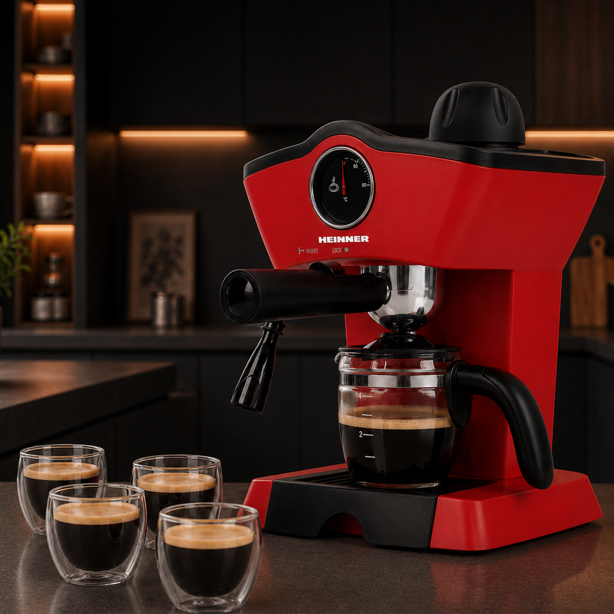 Machine à espresso Heinner rouge sur un comptoir avec quatre petites tasses en verre de café dans une cuisine sombre.