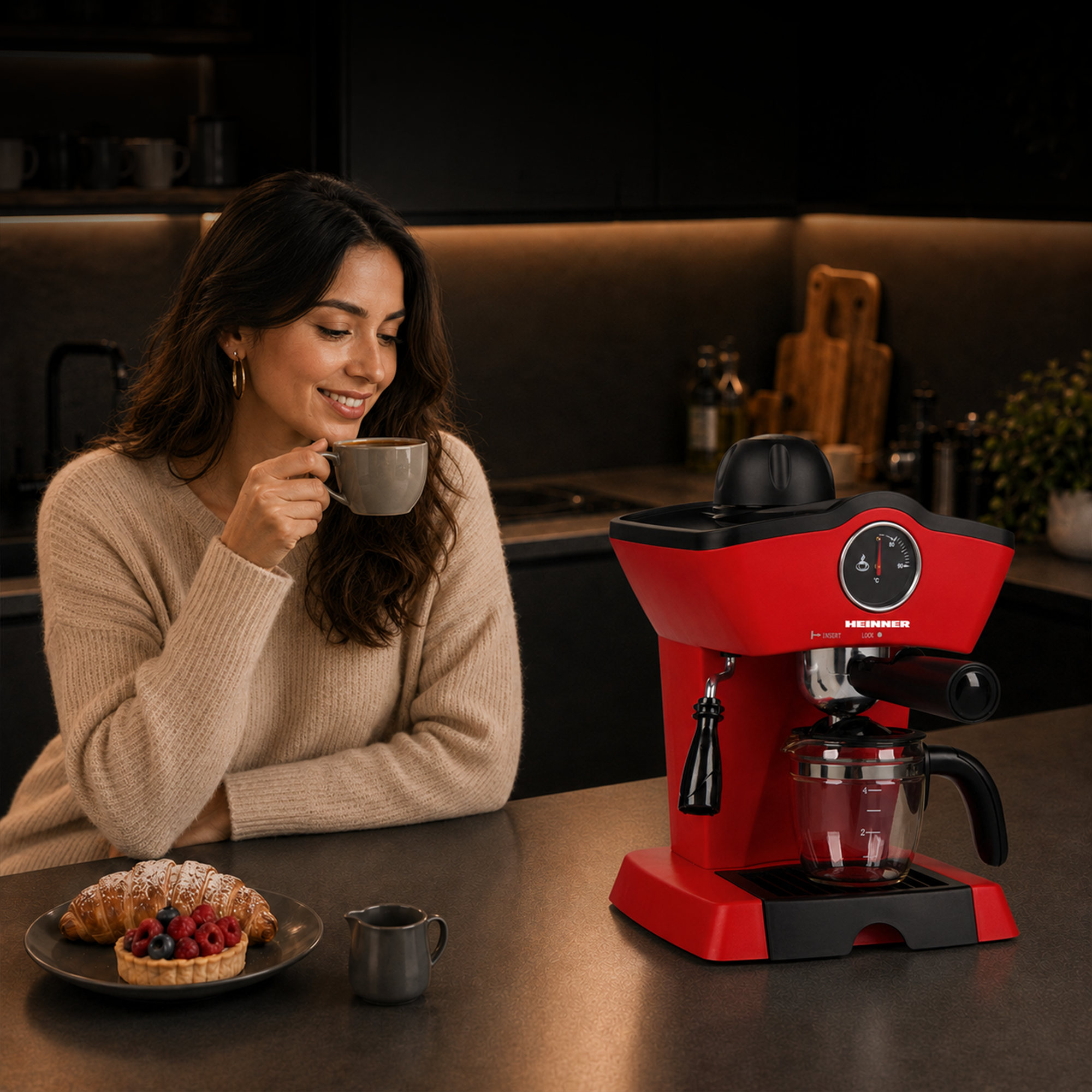 Une femme souriante est assise dans une cuisine à côté d'une machine à café rouge, tenant une tasse de café.