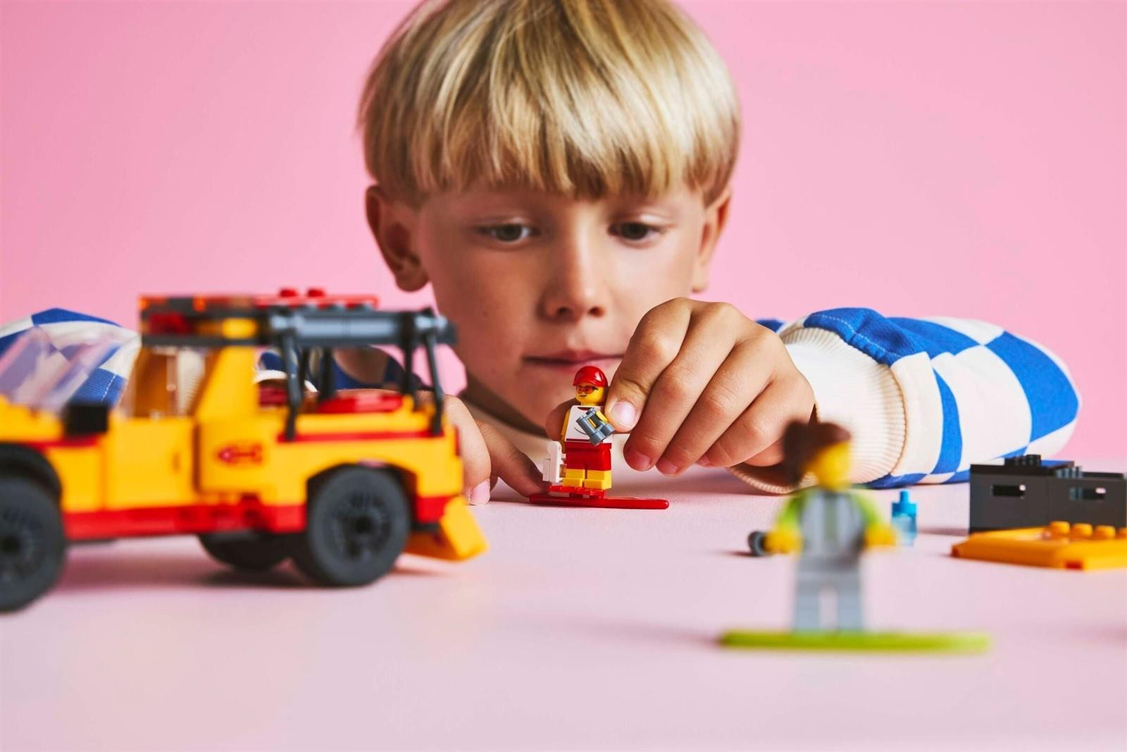 Ein Junge spielt an einem rosa Tisch mit Lego-Figuren und einem Spielzeugauto.