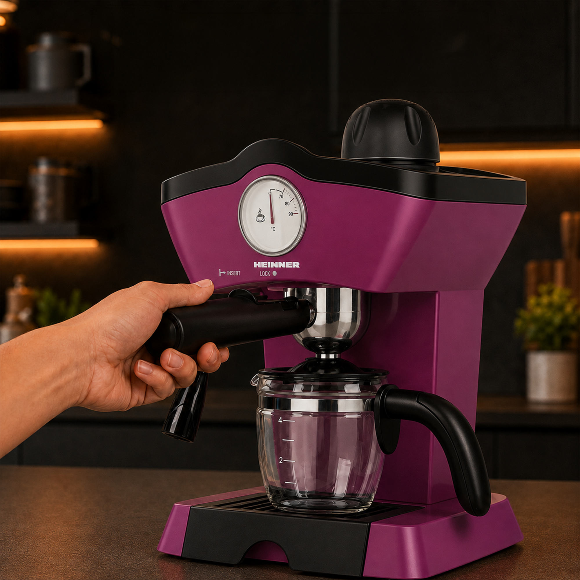 Eine Hand setzt den Siebträger in eine violette Heinner Espressomaschine ein, mit einer Glaskaraffe auf dem Tisch.