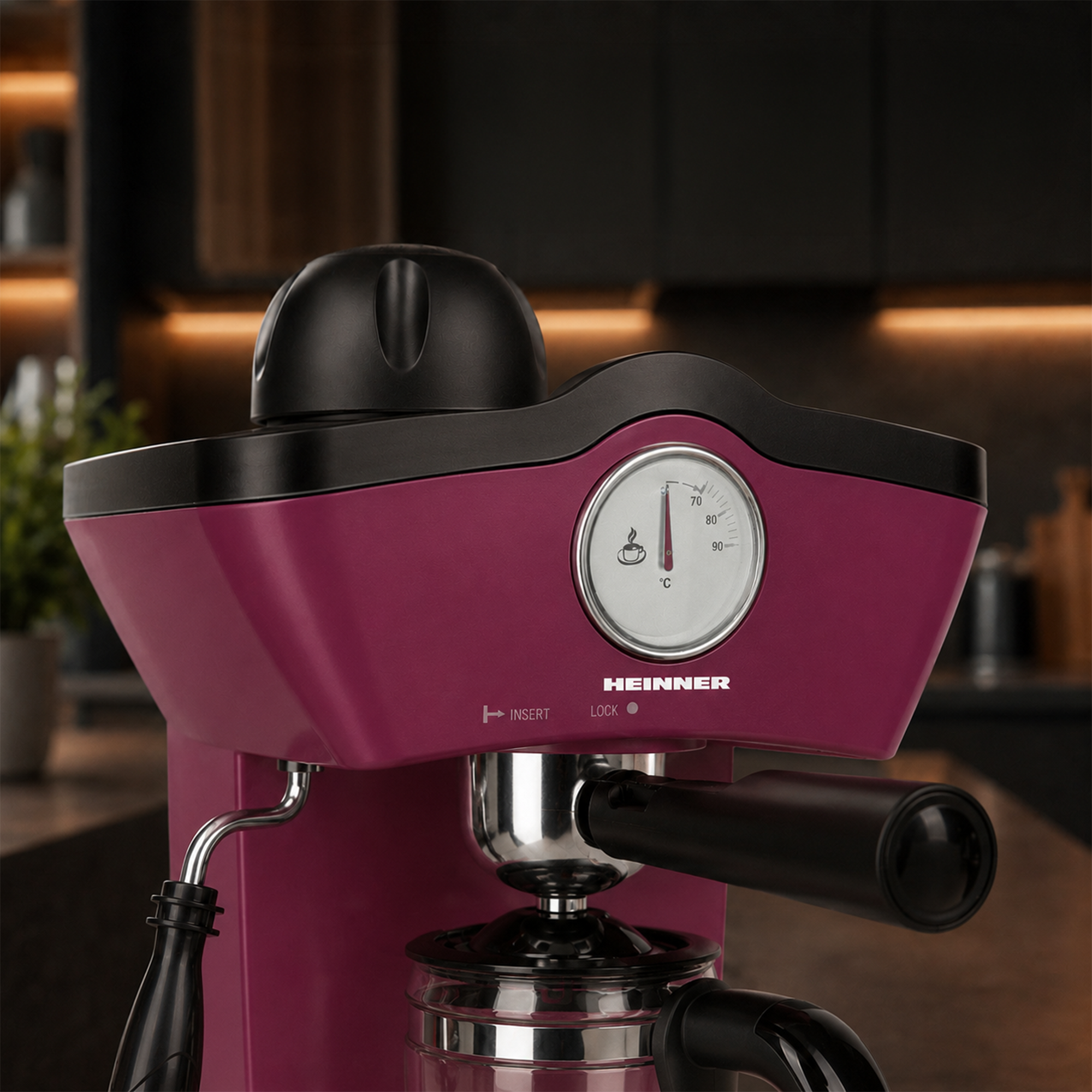 Eine pinke Heinner Espressomaschine mit Thermometer und schwarzem Griff in einer Küche.