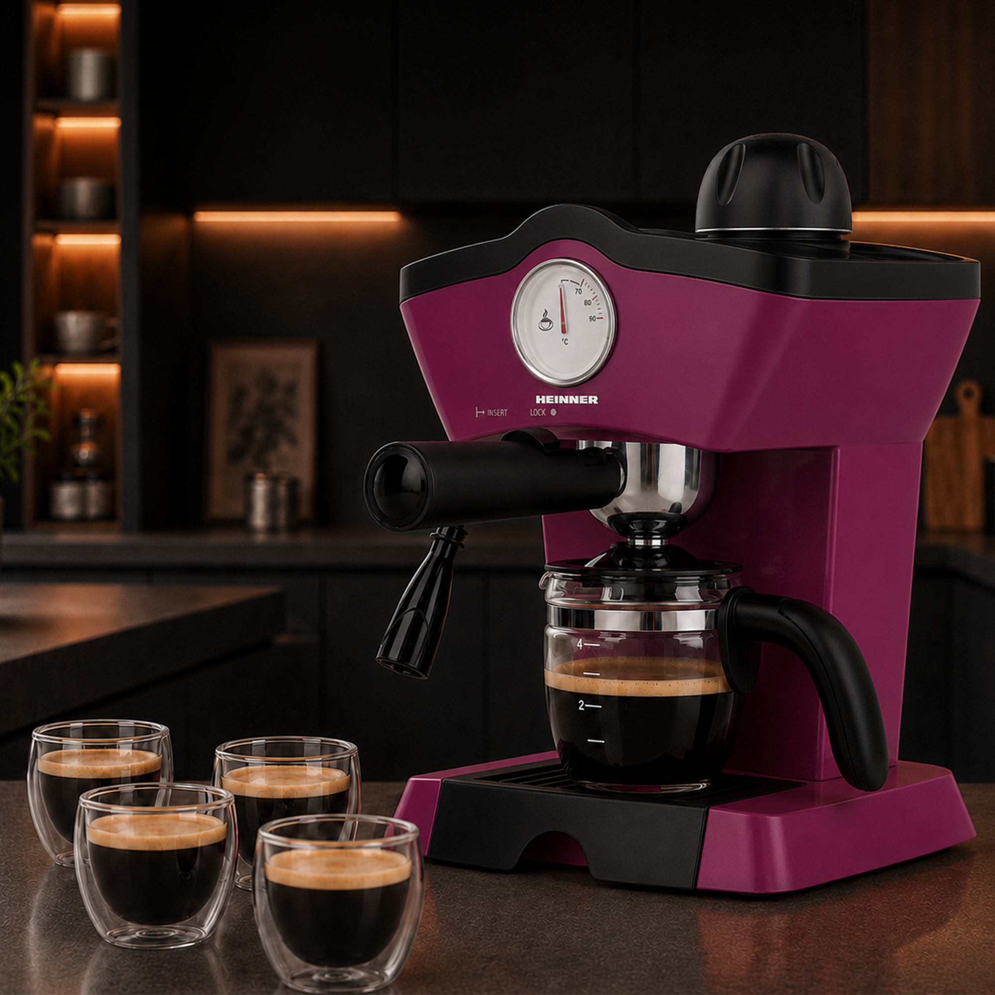Eine pinke Heinner Kaffeemaschine mit Glaskanne steht auf einer Theke, vier Espressotassen davor in einer Küche.