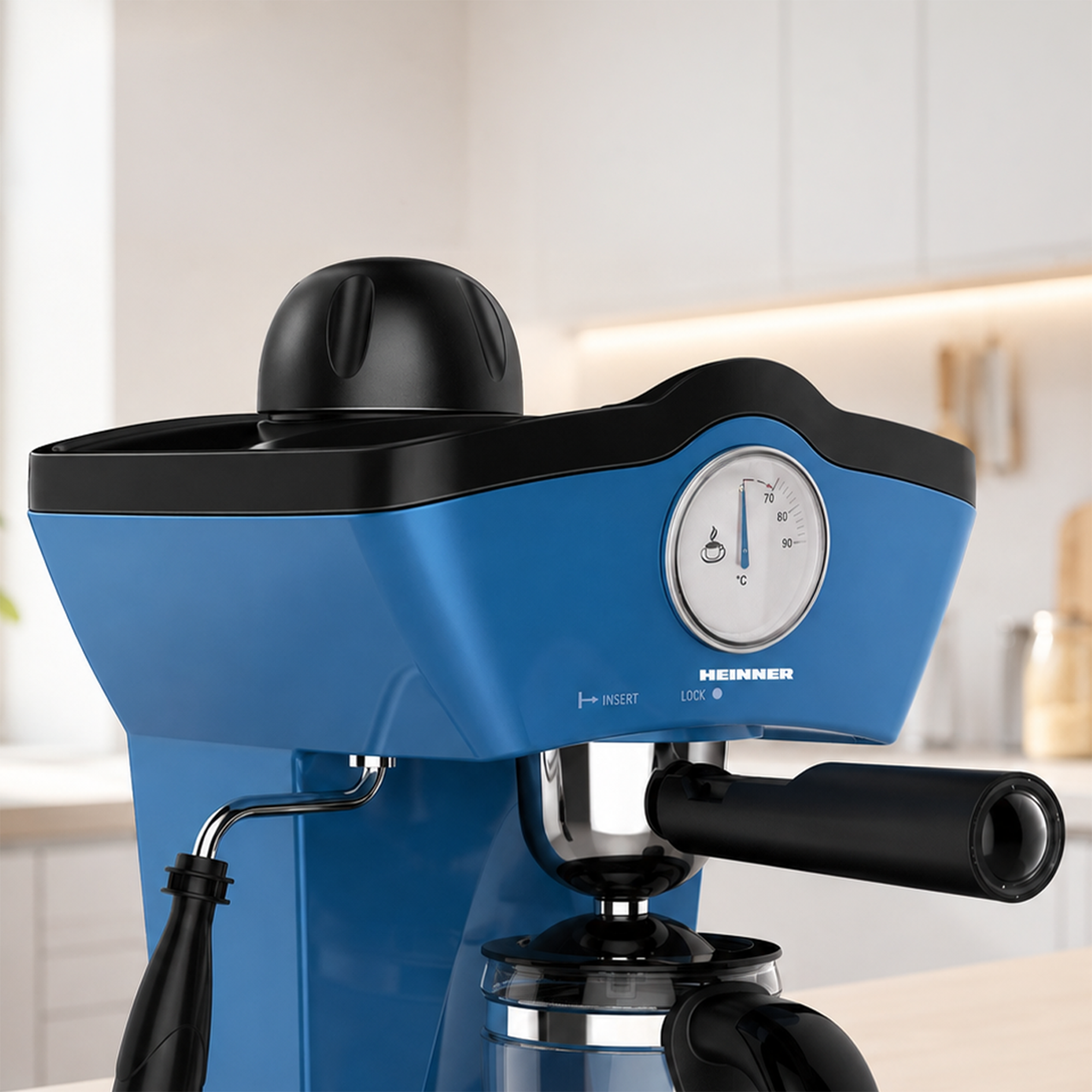 Blaue Espressomaschine mit schwarzem Griff, Temperaturanzeige und Glaskaraffe vor heller Küchenkulisse.