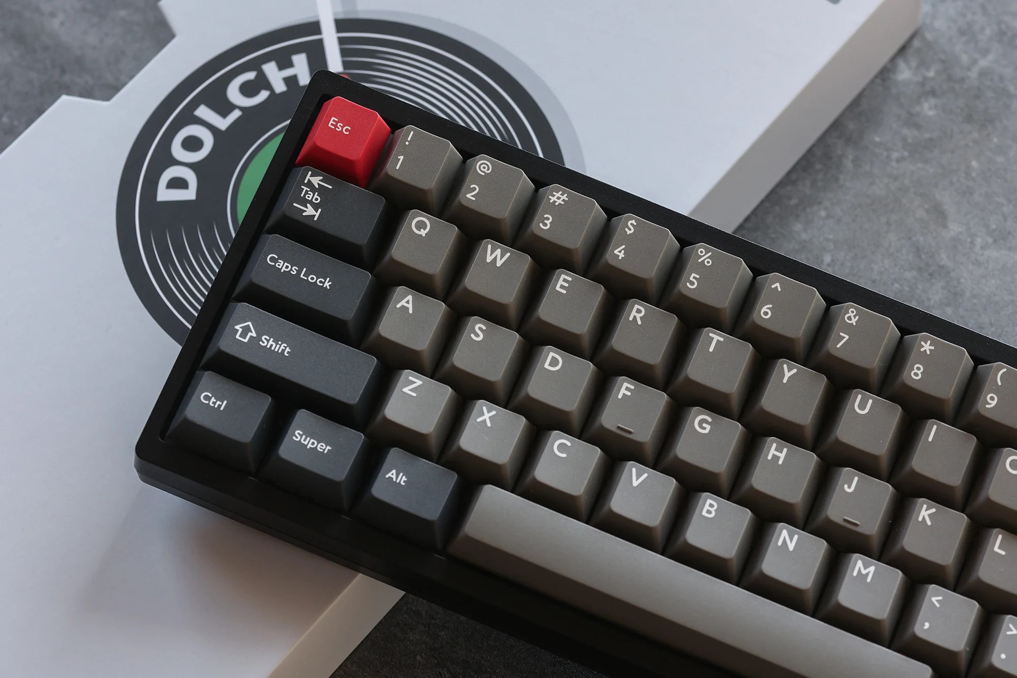 Mechaniczna klawiatura z szarymi klawiszami i czerwonym Esc leży na pudle Dolch.