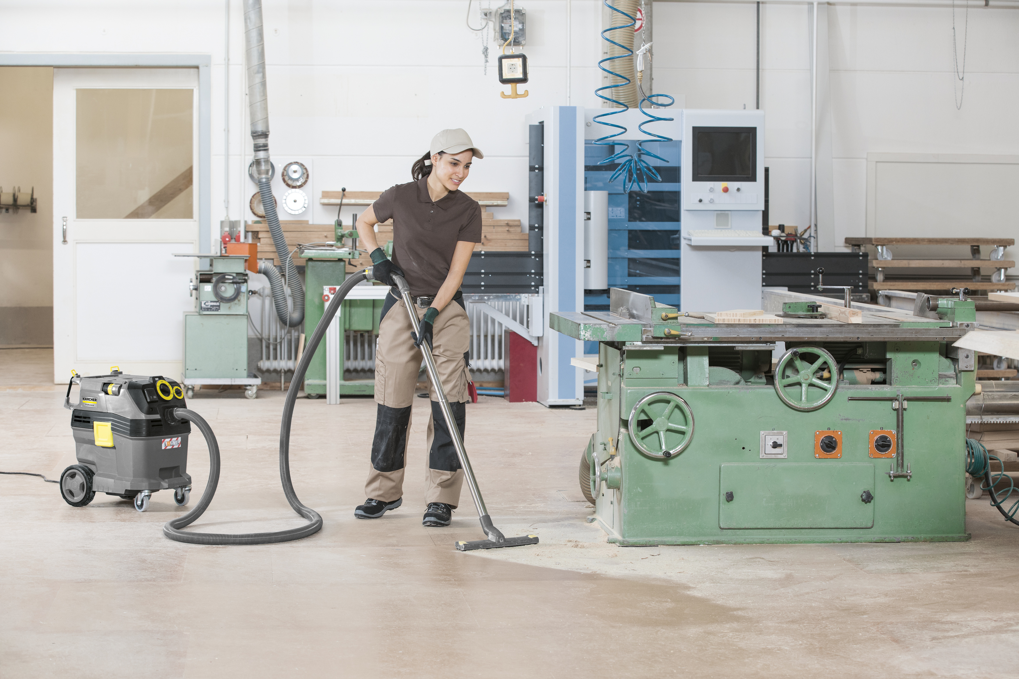 Eine Arbeiterin in einer Werkstatt saugt mit einem Industriestaubsauger den Holzboden.
