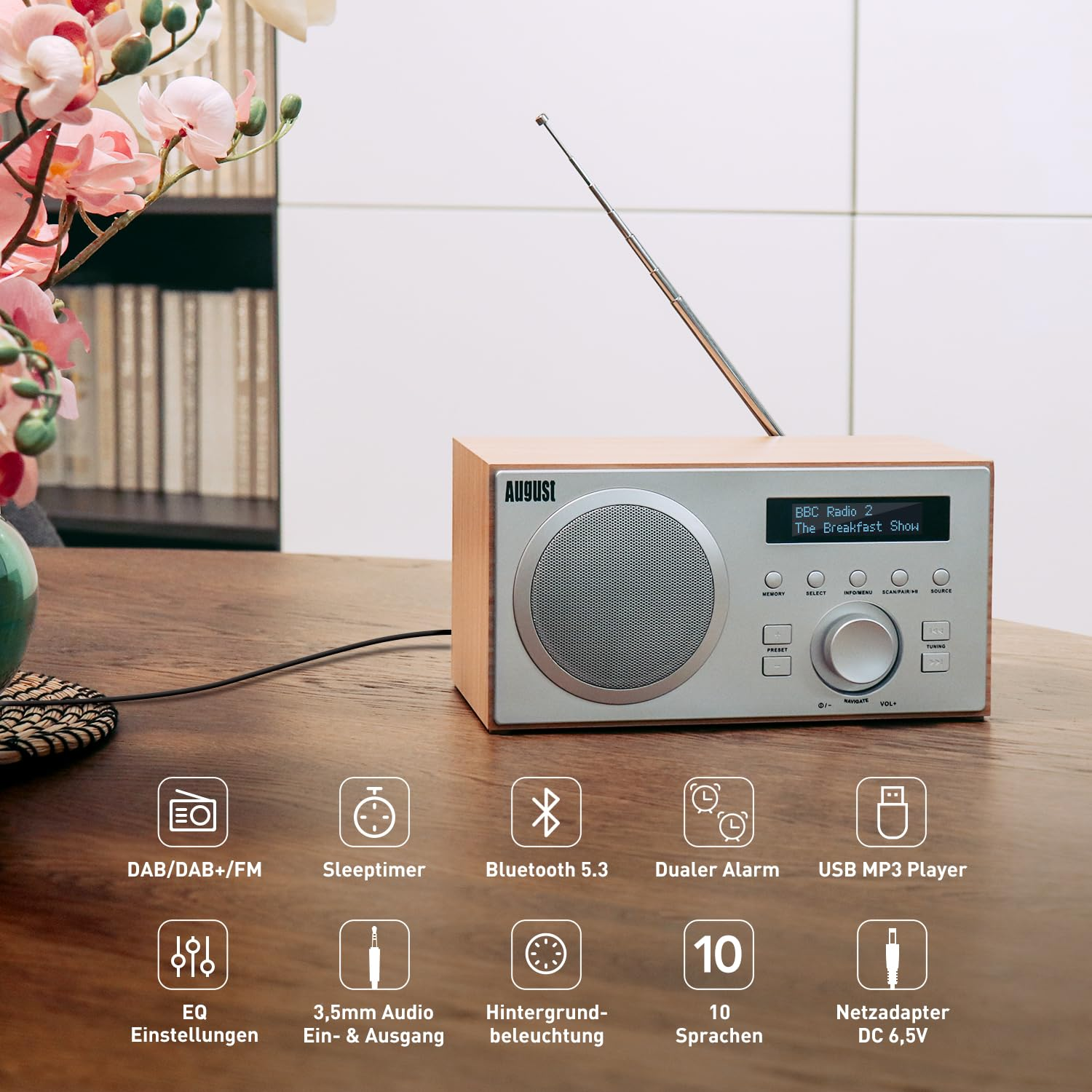 Radio effetto legno con frontale in metallo, antenna, display e tasti, su tavolo in legno con icone di funzioni.