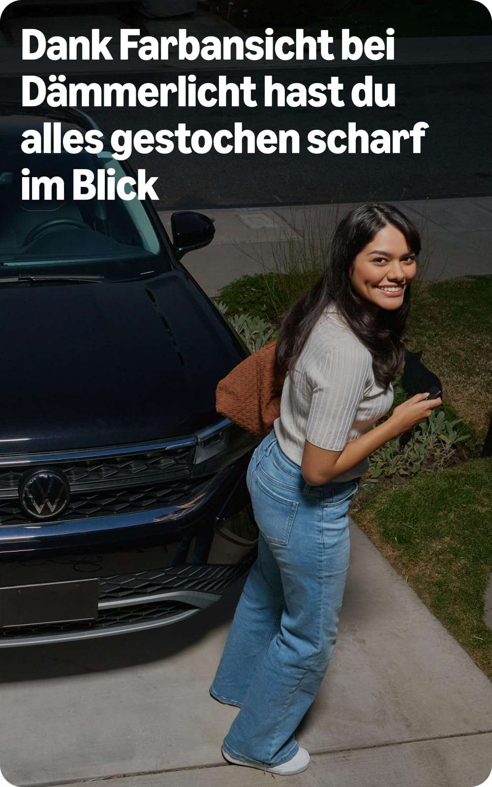 Una donna sorridente si trova al crepuscolo accanto a un'auto nera.