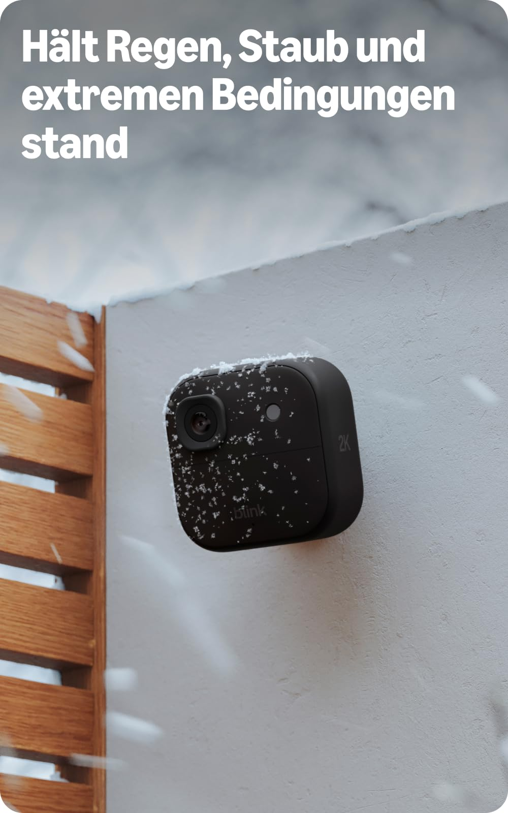 Una telecamera di sicurezza Blink nera montata su un muro inneggiato all'aperto con neve che cade.