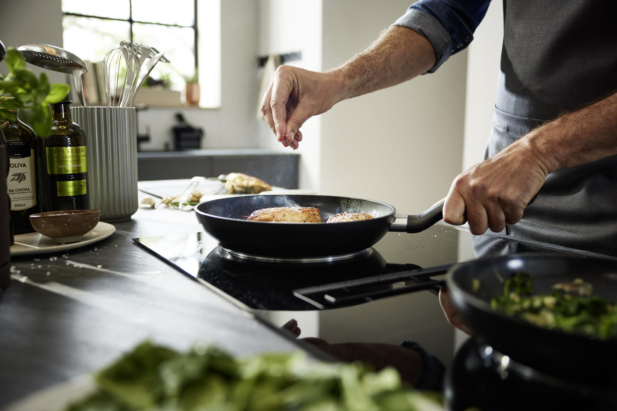 Une personne dans une cuisine assaisonne des aliments dans une poêle sur une plaque à induction.