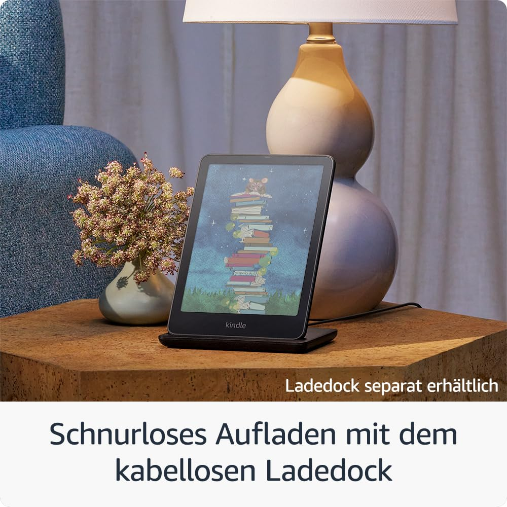 Un Kindle sur station de charge, avec lampe, vase de fleurs et fauteuil bleu en arrière-plan sur une table en bois.