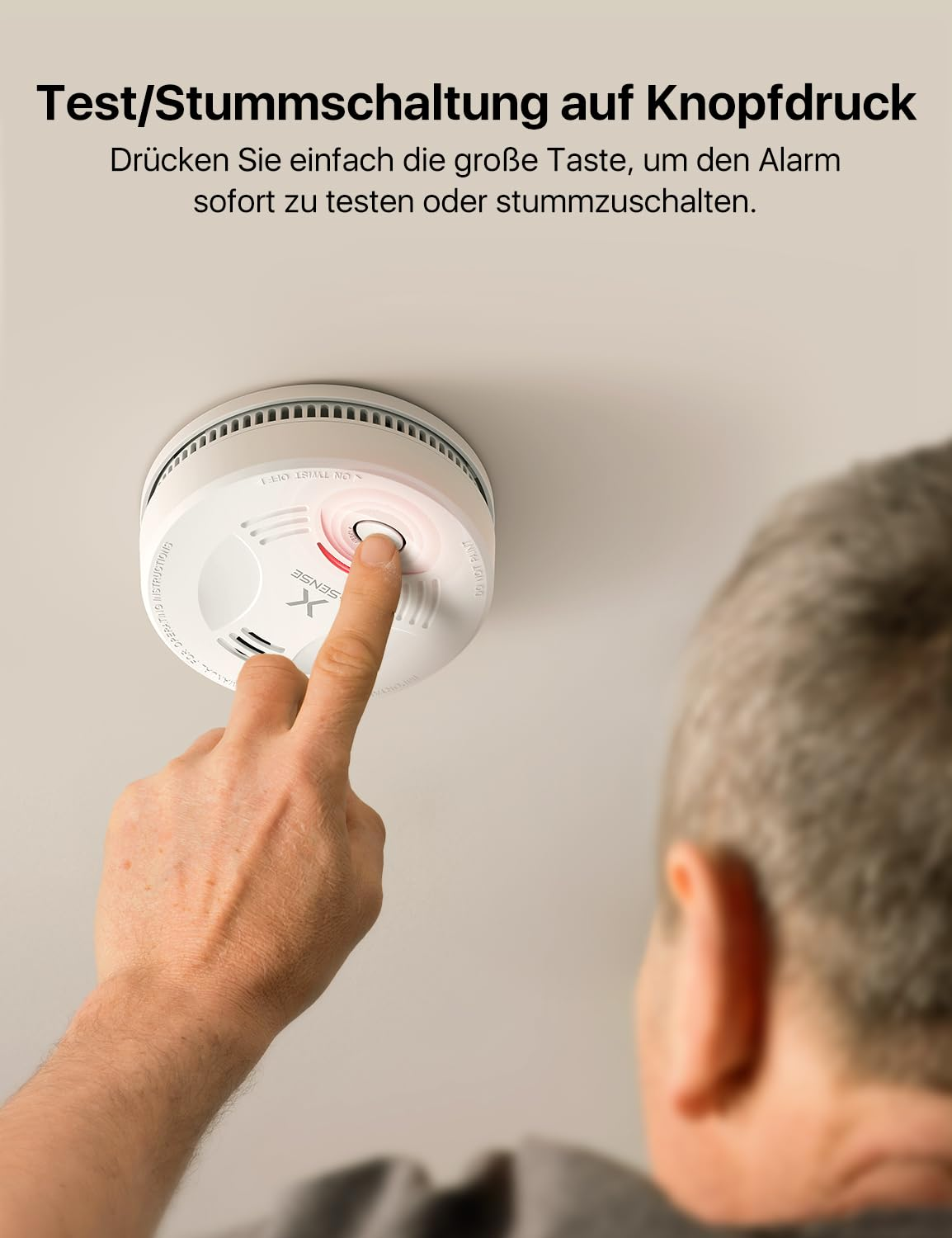 Un homme appuyant sur le grand bouton d'un détecteur de fumée blanc au plafond.