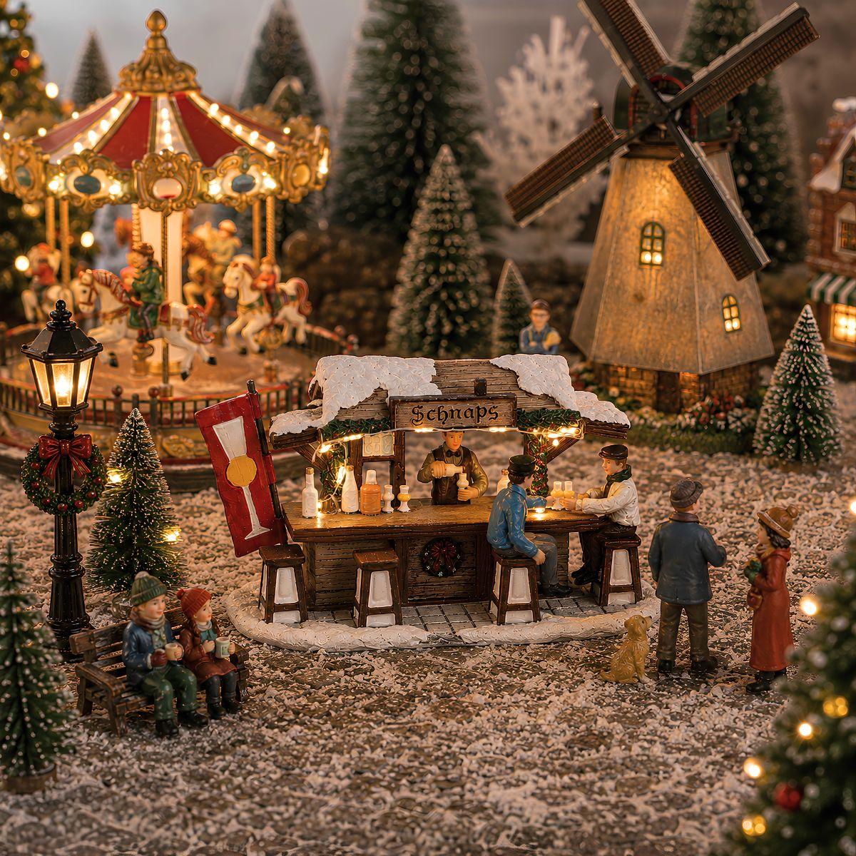 Marché de Noël miniature avec stand de schnaps illuminé, carrousel, moulin et arbres enneigés.