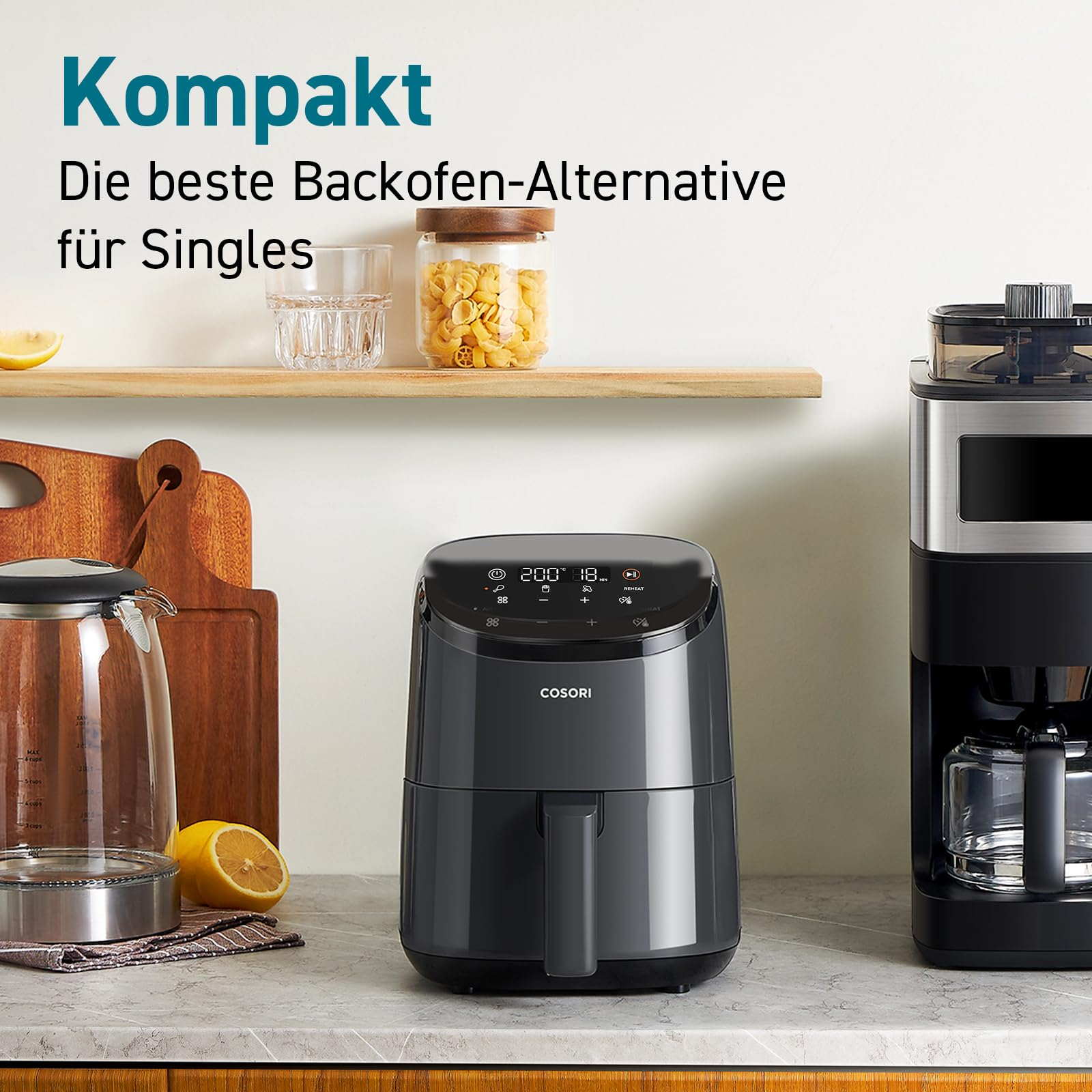 Une friteuse à air Cosori grise sur un comptoir de cuisine avec cafetière, bouilloire et texte publicitaire allemand.