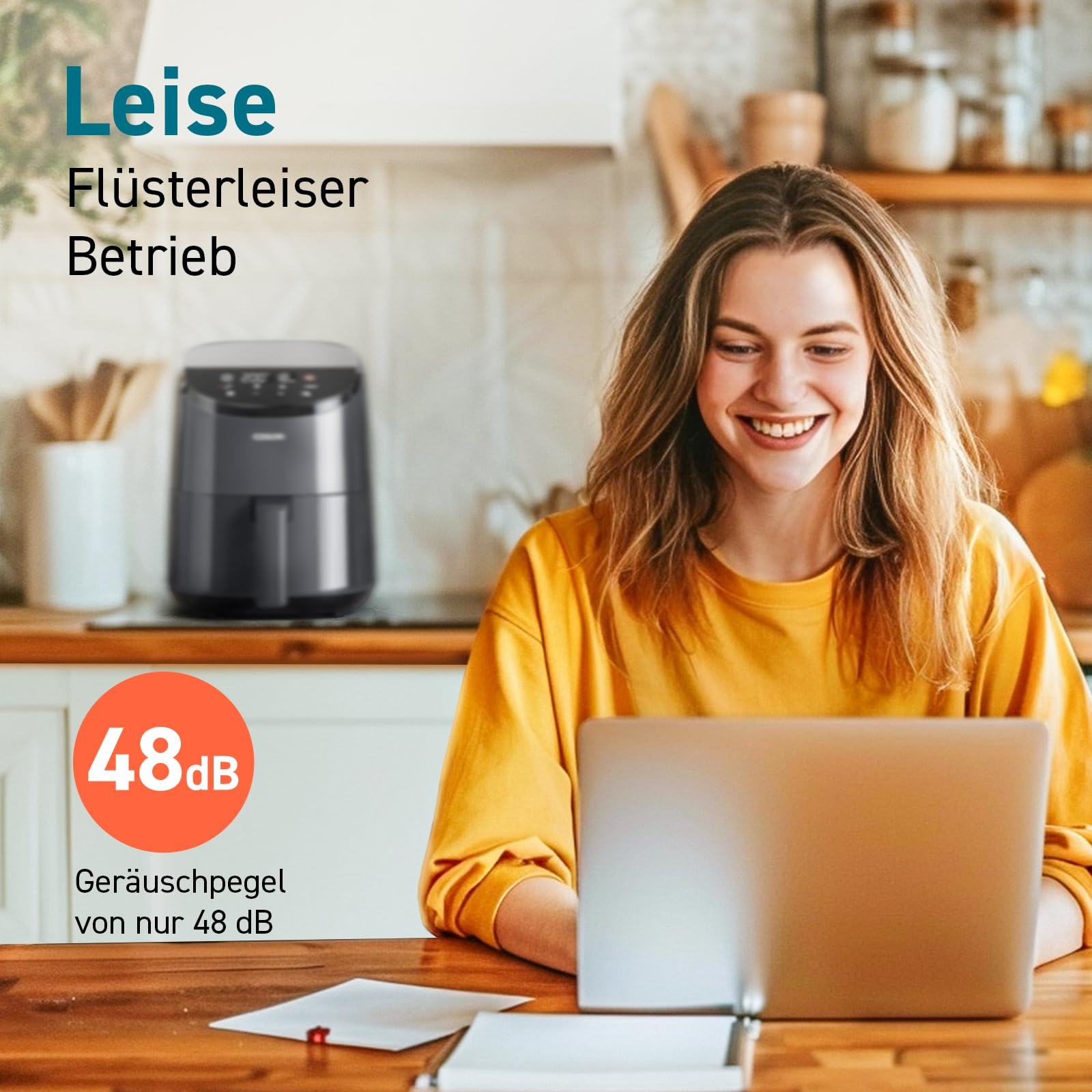 Une femme souriante travaille sur un ordinateur portable dans une cuisine avec une friteuse.