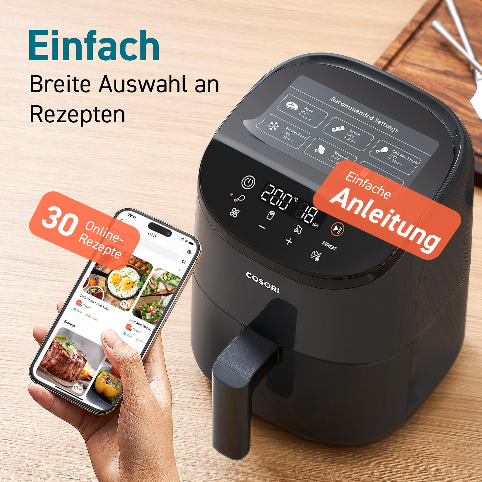 Friteuse à air Cosori noire sur une table près d'une main tenant un smartphone.