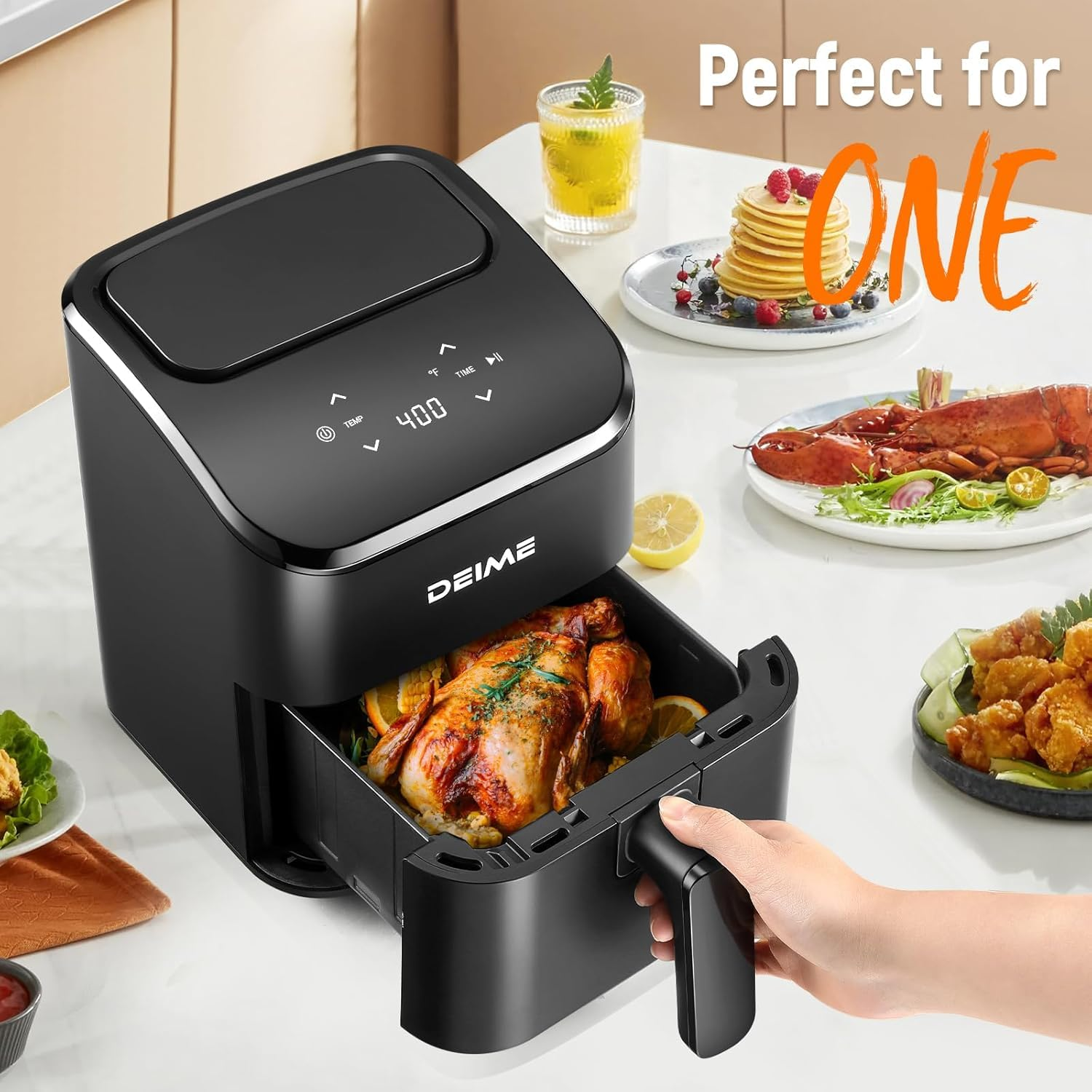 Une friteuse à air noire Deime montre un poulet entier rôti dans son panier ouvert sur une table remplie de nourriture.